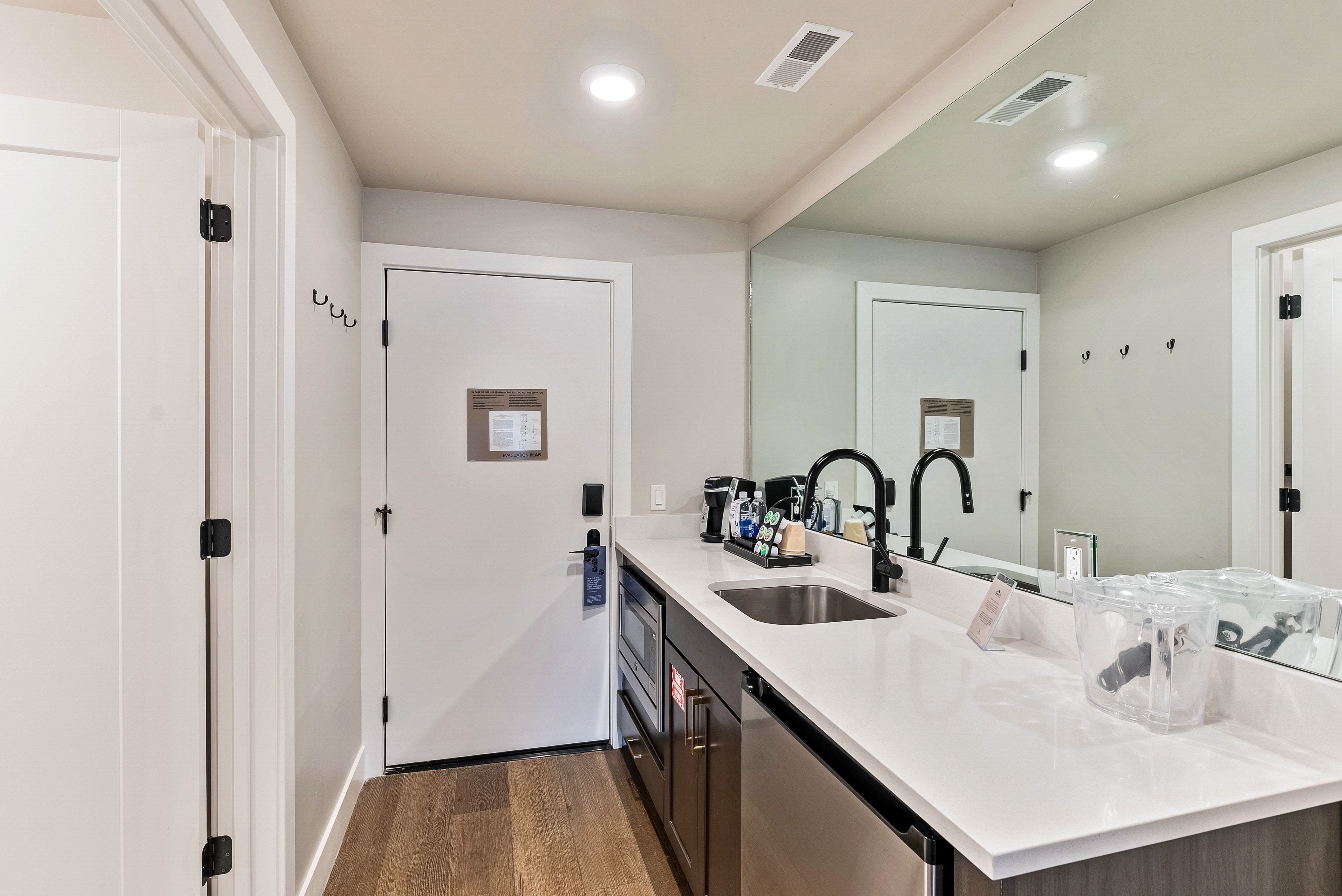 Modern kitchenette featuring a stainless steel sink, black gooseneck faucet, white countertop, and wood-finish flooring