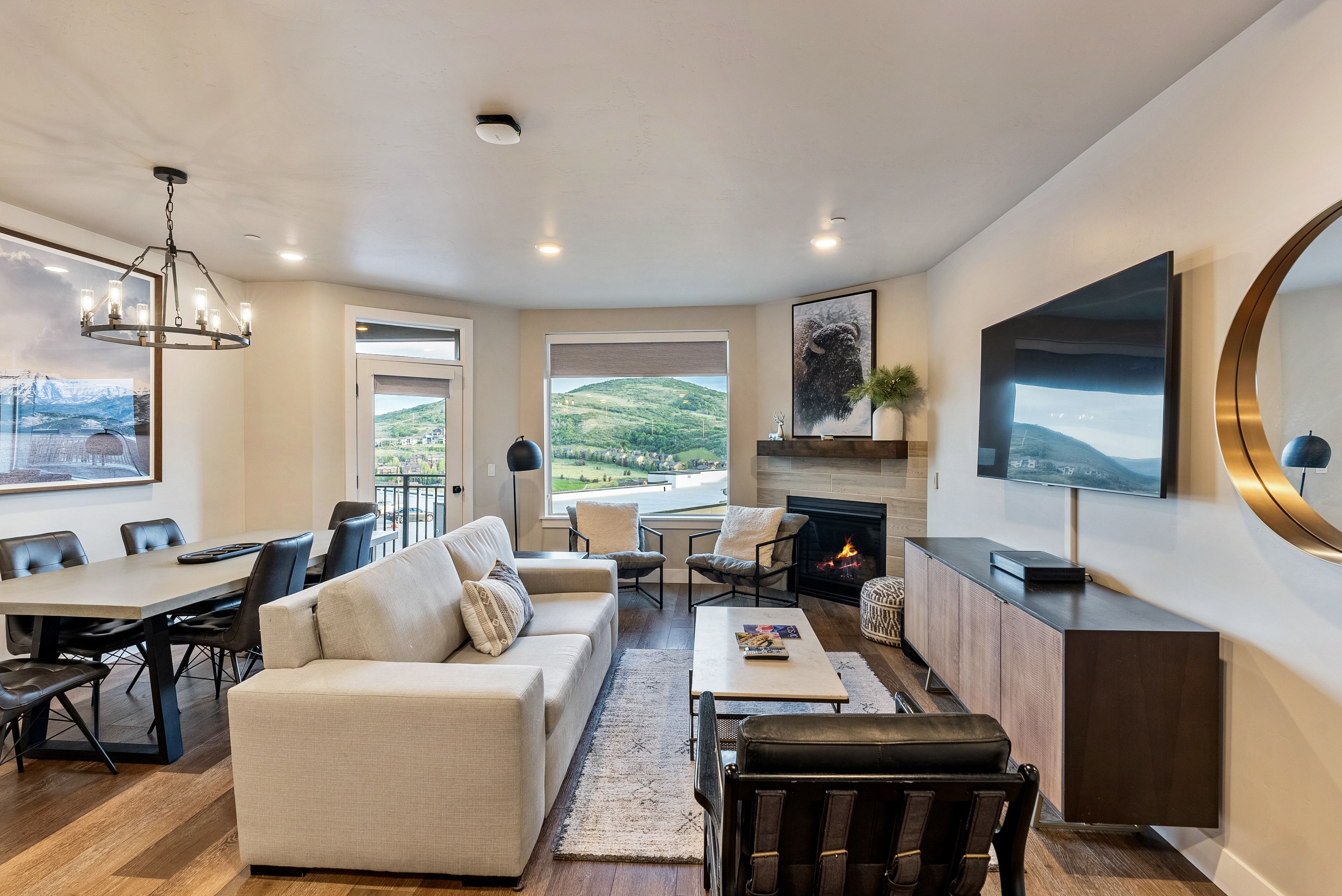 Spacious living area featuring wood-finish flooring, a contemporary fireplace with a wood mantel, and large windows offering expansive mountain scenery