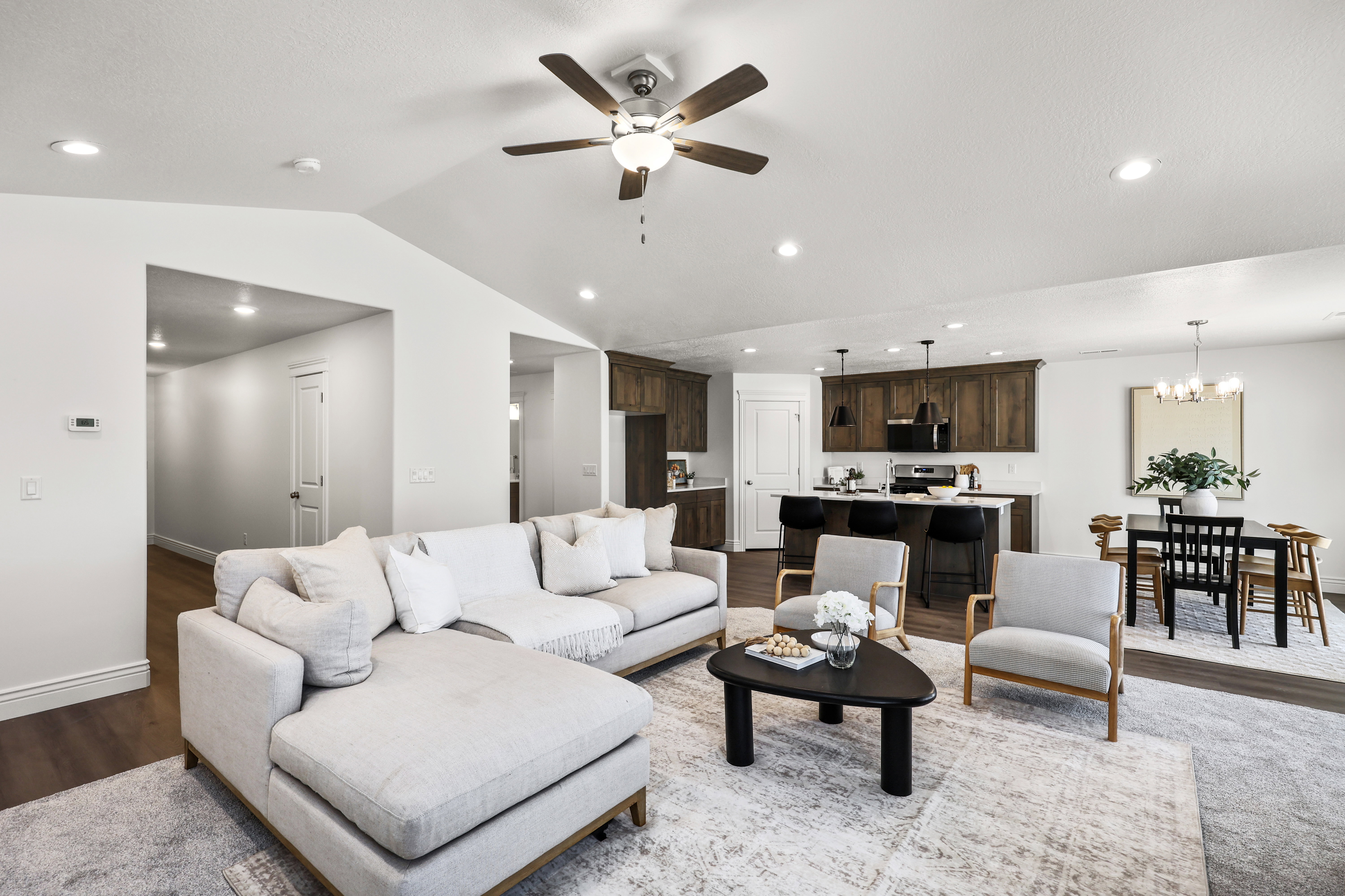 Open-concept living area featuring wood-finish flooring, recessed lighting, a ceiling fan, and access to a kitchen with dark wood cabinetry and a central island