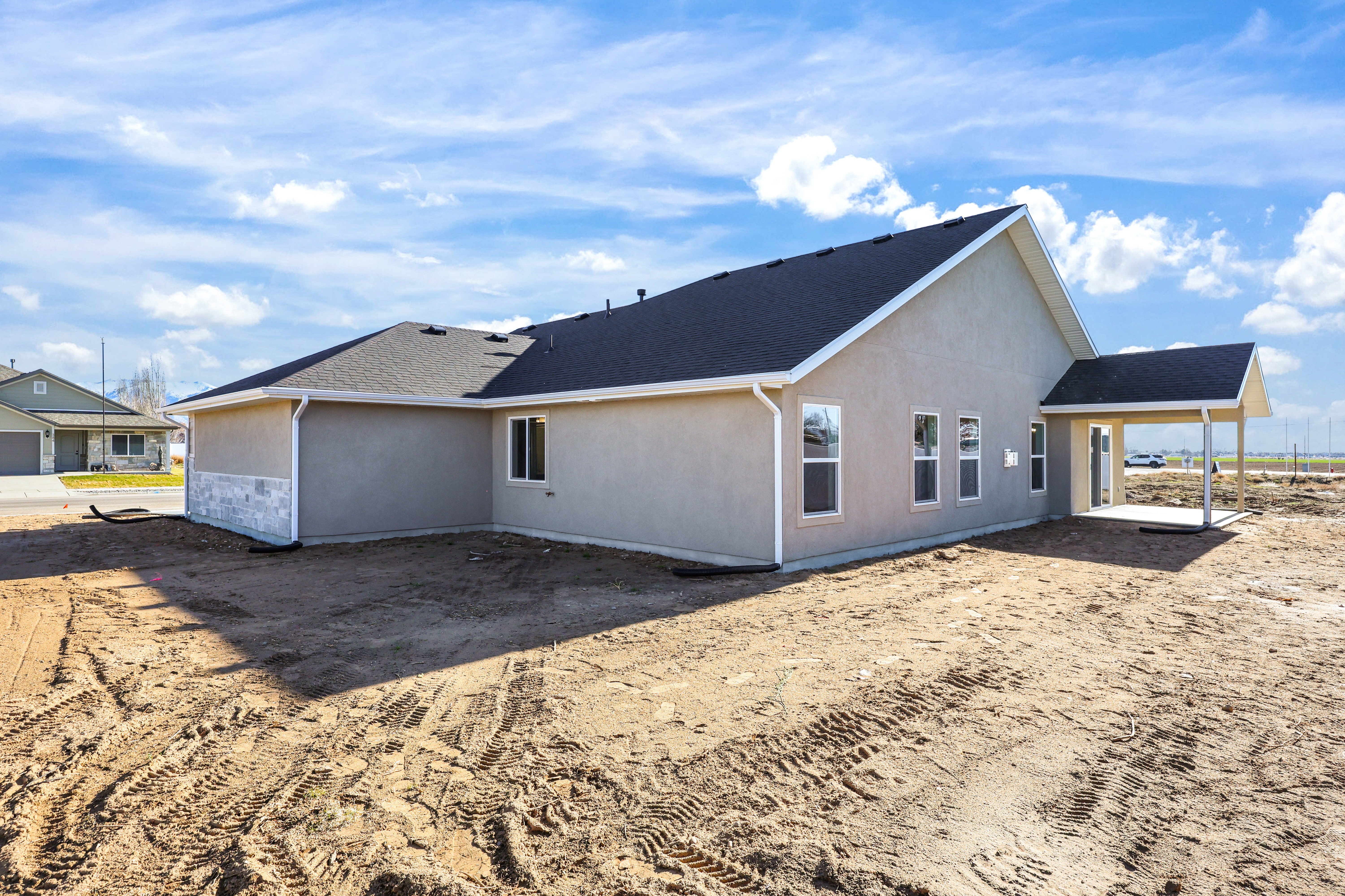 Contemporary stucco exterior featuring a dark asphalt shingle roof, white window trim, and a covered back patio