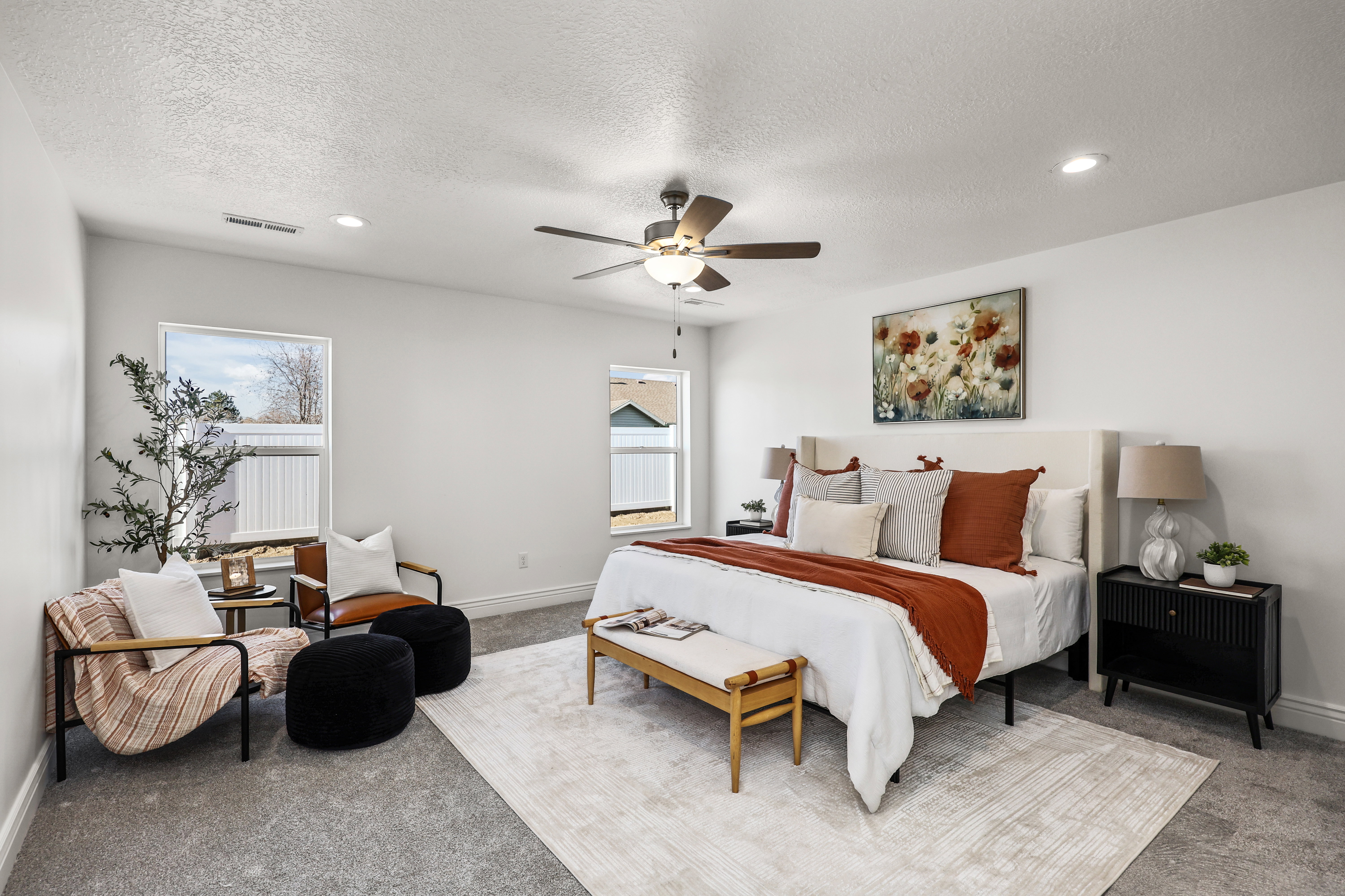 Spacious bedroom featuring light gray carpeting, crisp white walls, multiple windows providing natural light, a ceiling fan with integrated lighting, and recessed ceiling lights