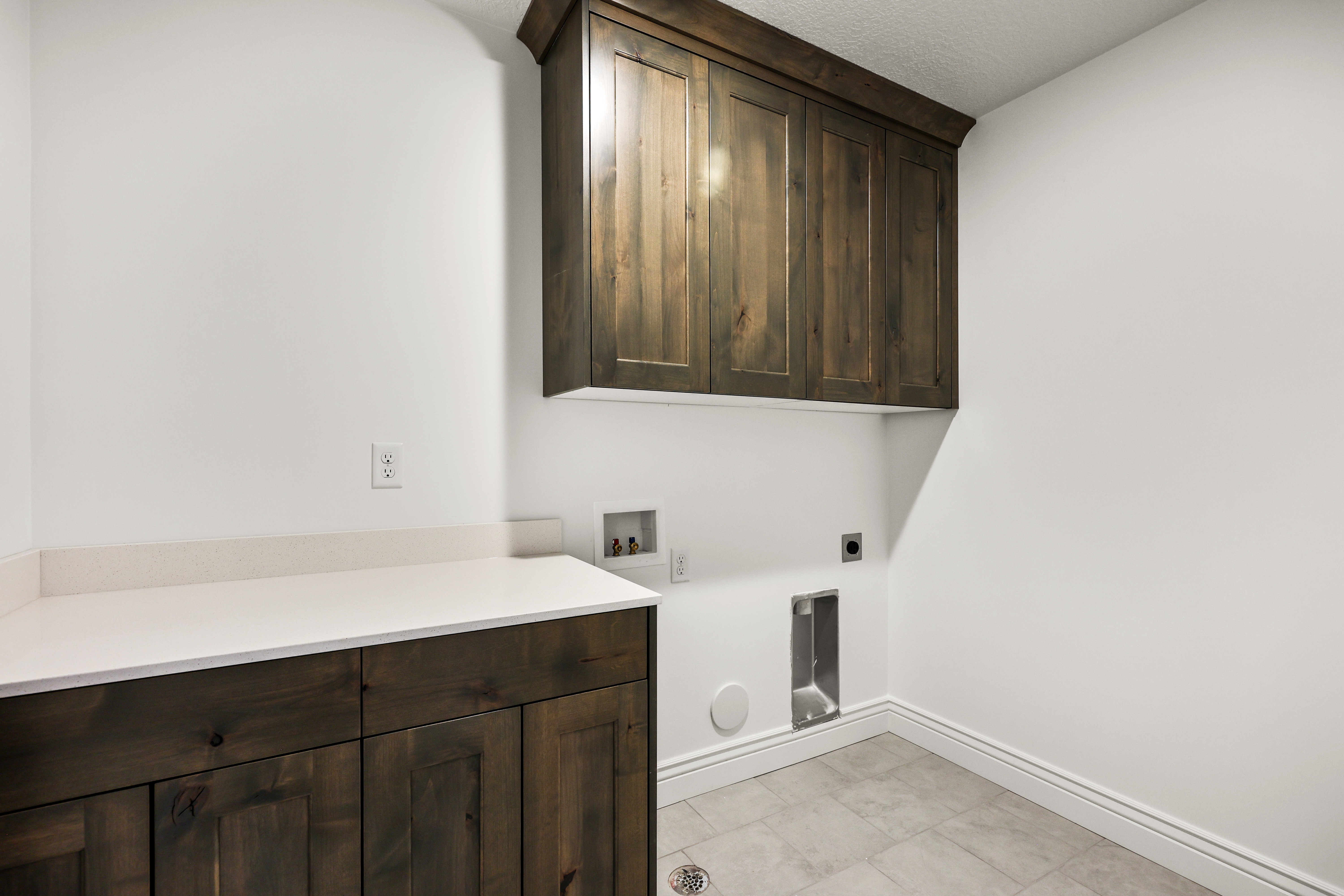 Laundry area featuring wood-finish cabinetry, a light-toned countertop, and tiled flooring