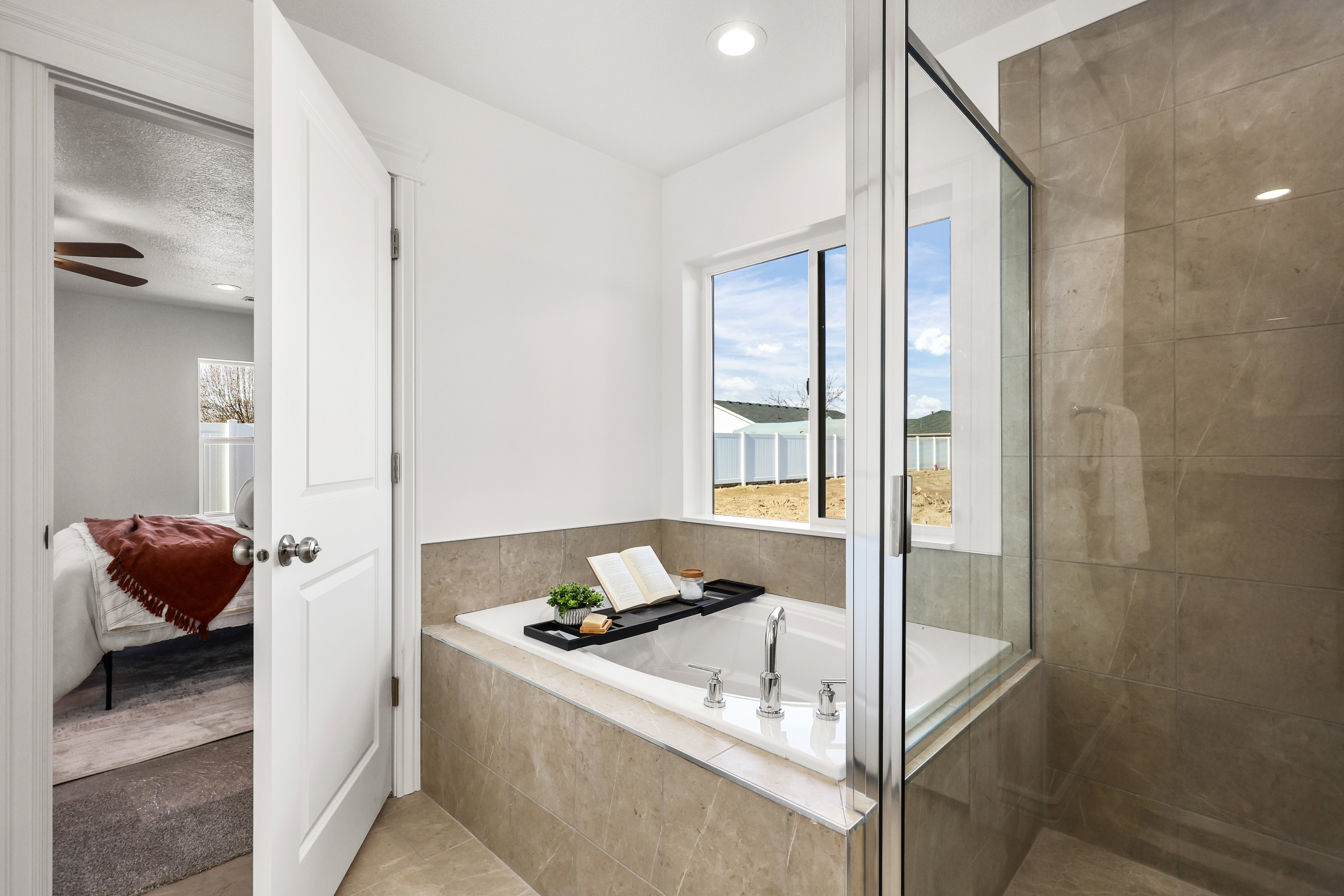 Bathroom featuring a built-in soaking tub with deck-mounted fixtures, a glass-enclosed shower with full-height tile, and a large window providing natural light