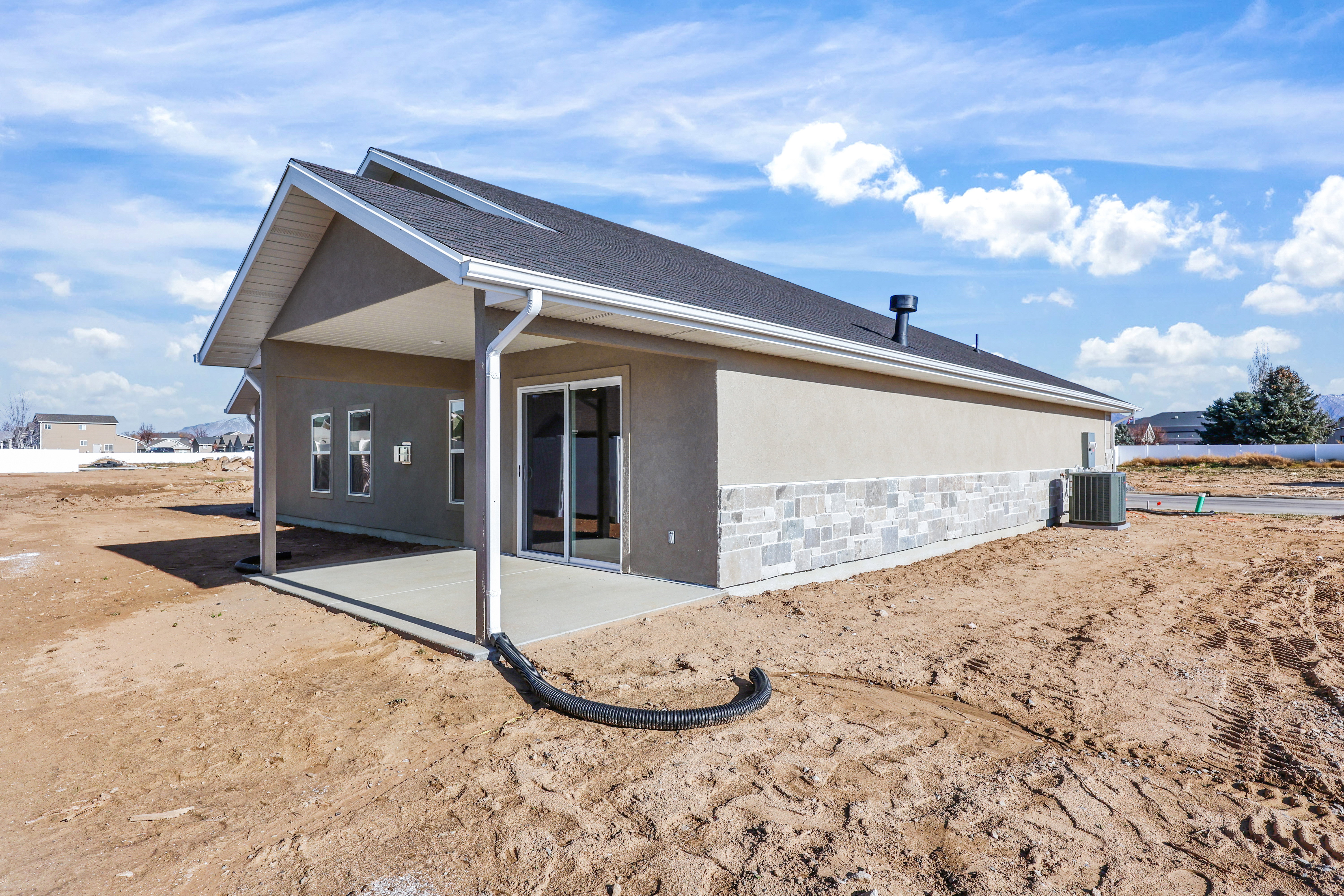 Rear exterior featuring a covered concrete patio, sliding glass doors, and multiple windows