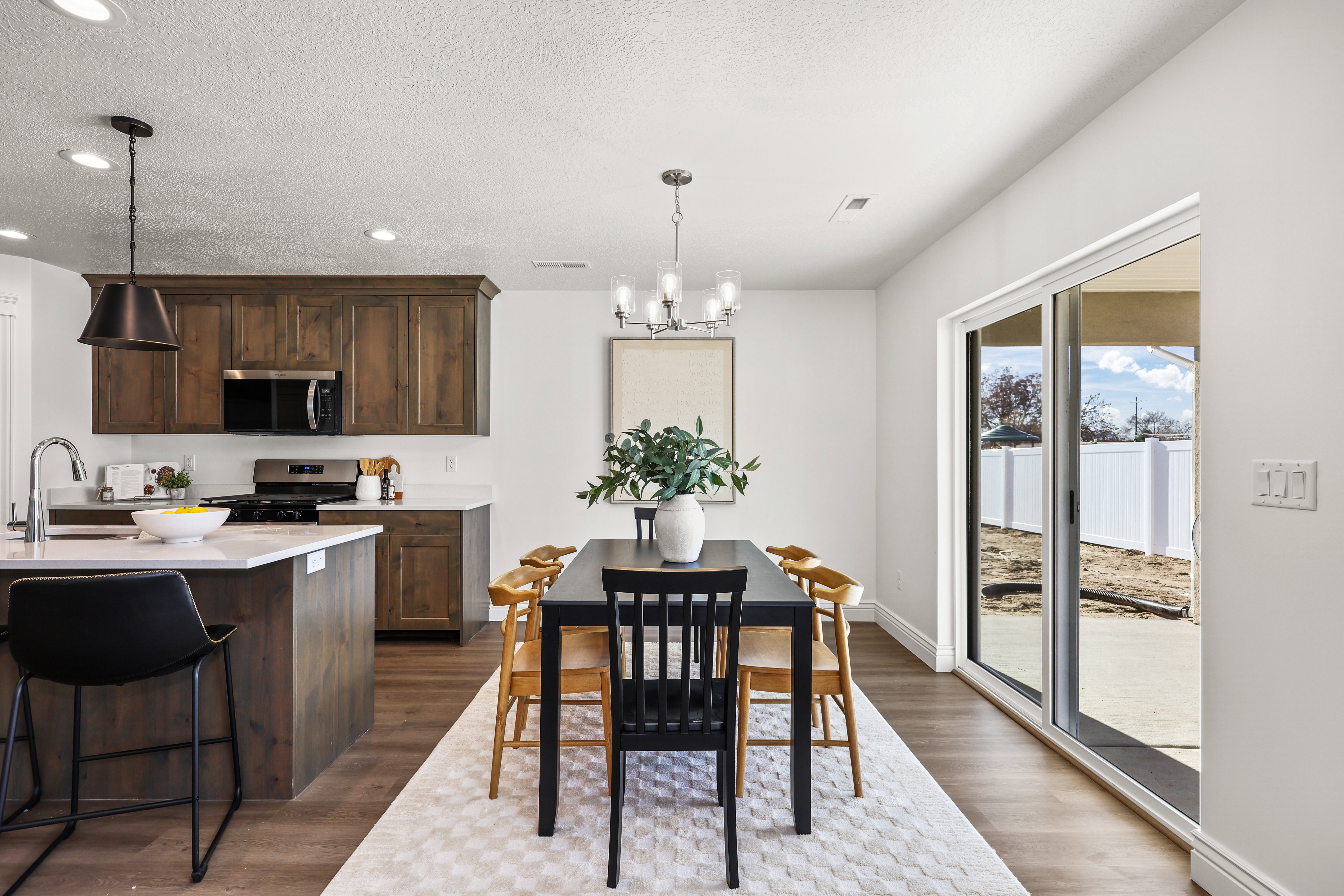 Open-concept kitchen and dining area featuring rich wood cabinetry, stainless steel appliances, a kitchen island with seating, wood-finish flooring, and a sliding glass door leading to a patio