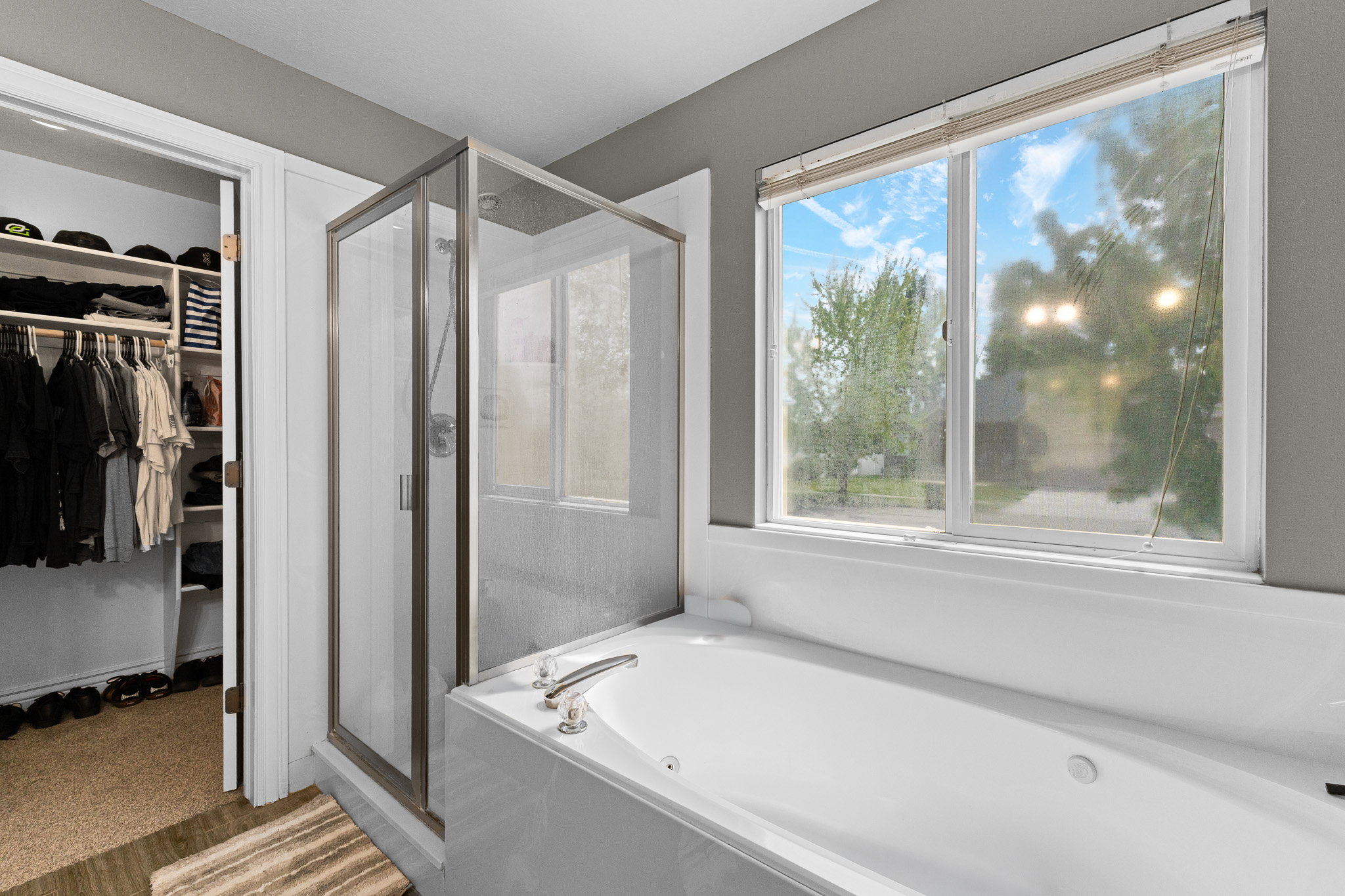 Soaking tub with brushed nickel fixtures, a glass-enclosed shower, and an adjacent walk-in closet with built-in shelving