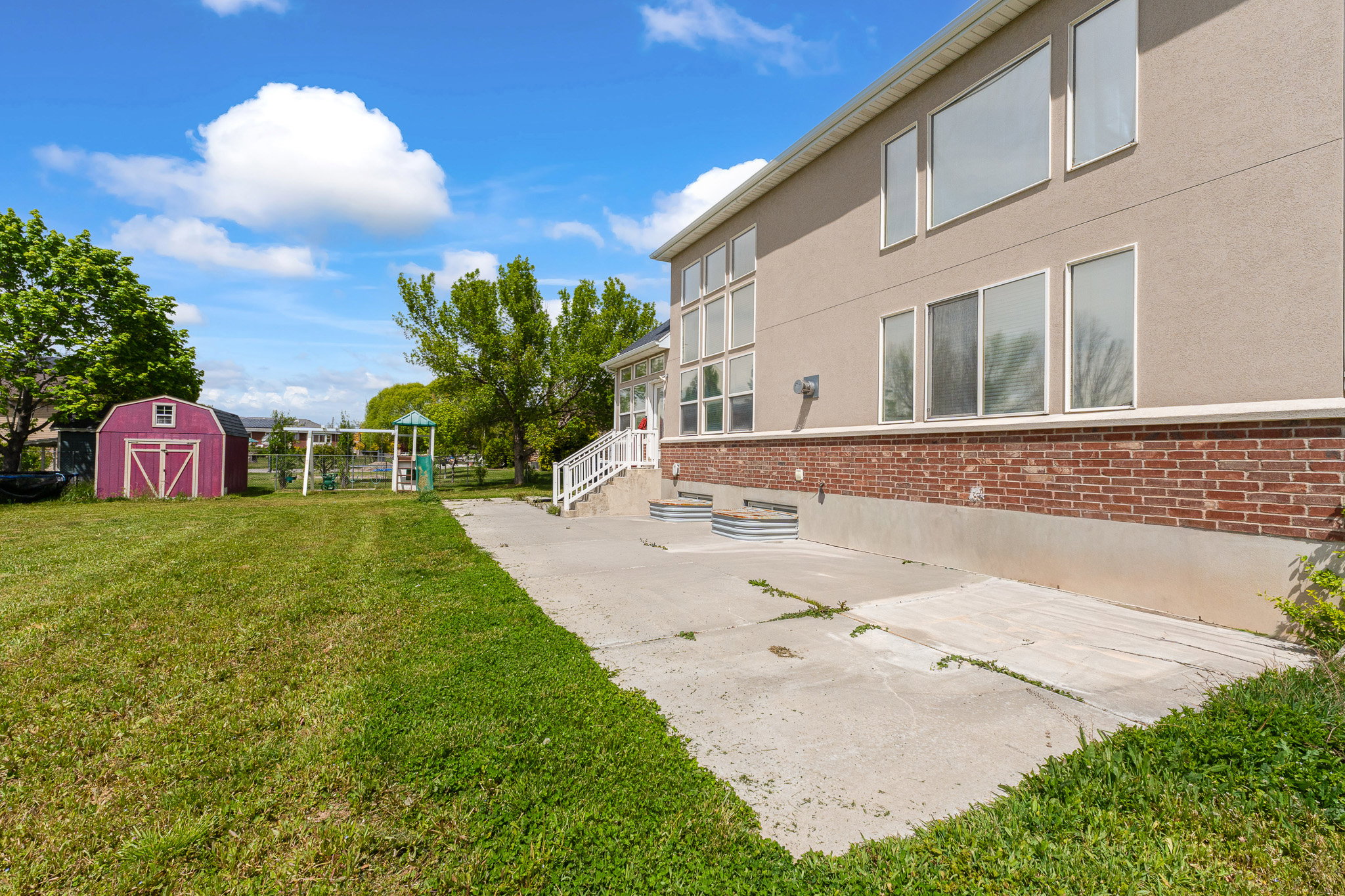 Expansive lawn featuring a storage shed, concrete patio, and a swing set