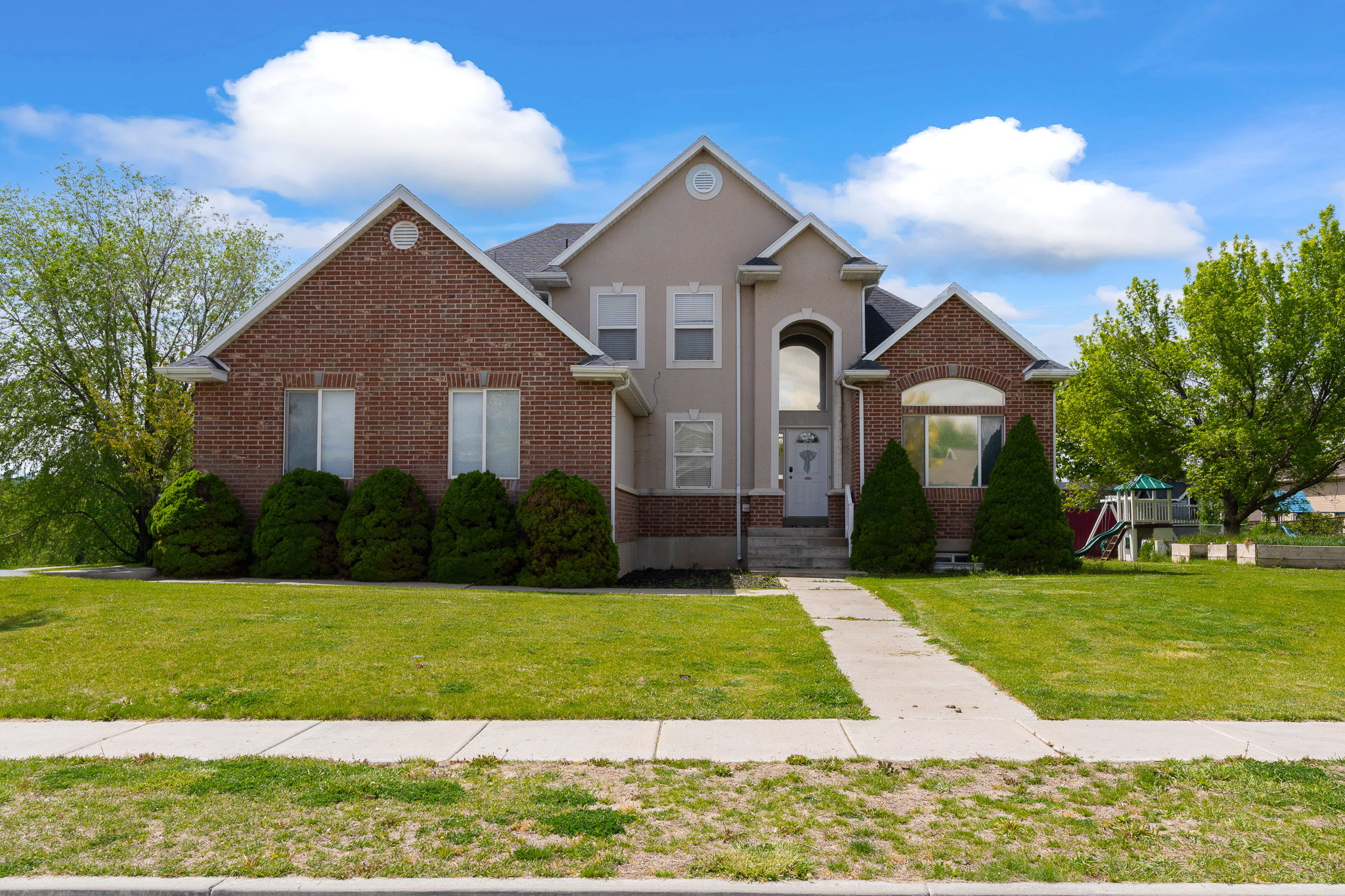 Brick and stucco exterior residence featuring a front lawn and a concrete walkway