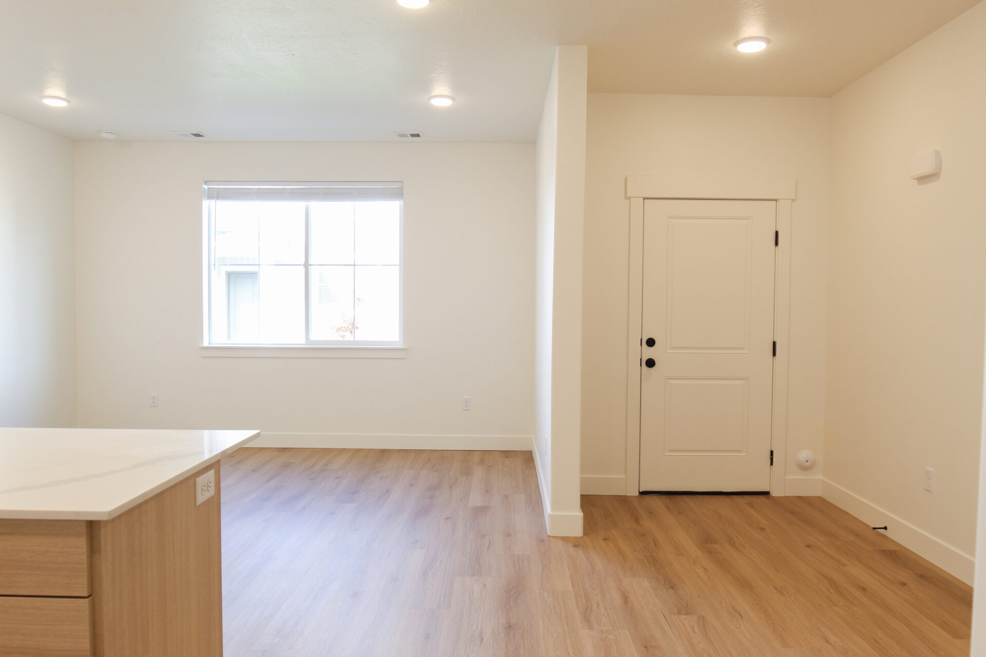 Open-concept interior featuring light wood-finish flooring, recessed lighting, white walls, and a contemporary kitchen island with a light-toned countertop