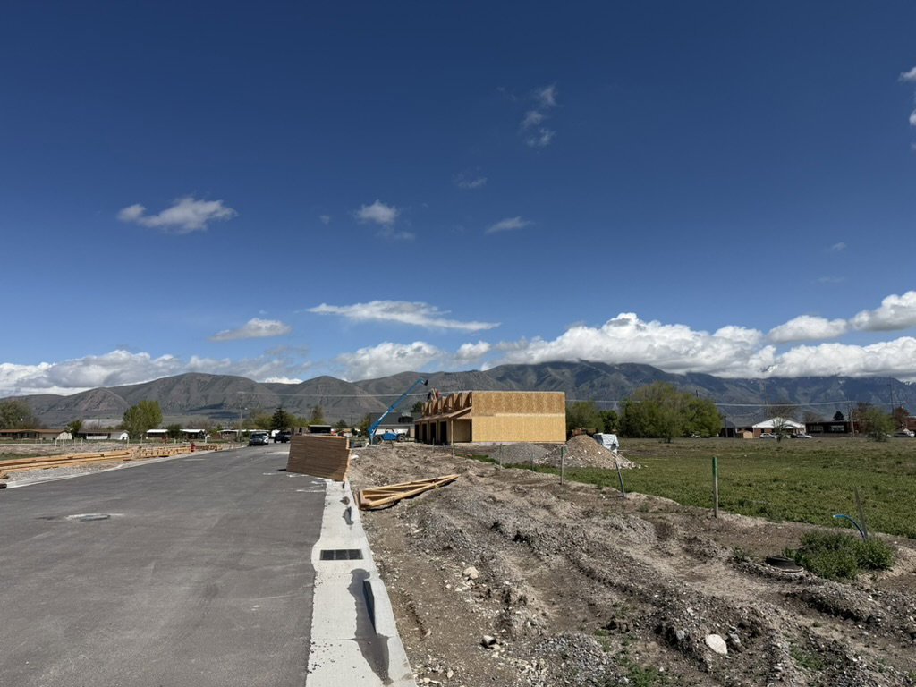 New construction framing visible, featuring a mountain backdrop, paved street, and developing lot