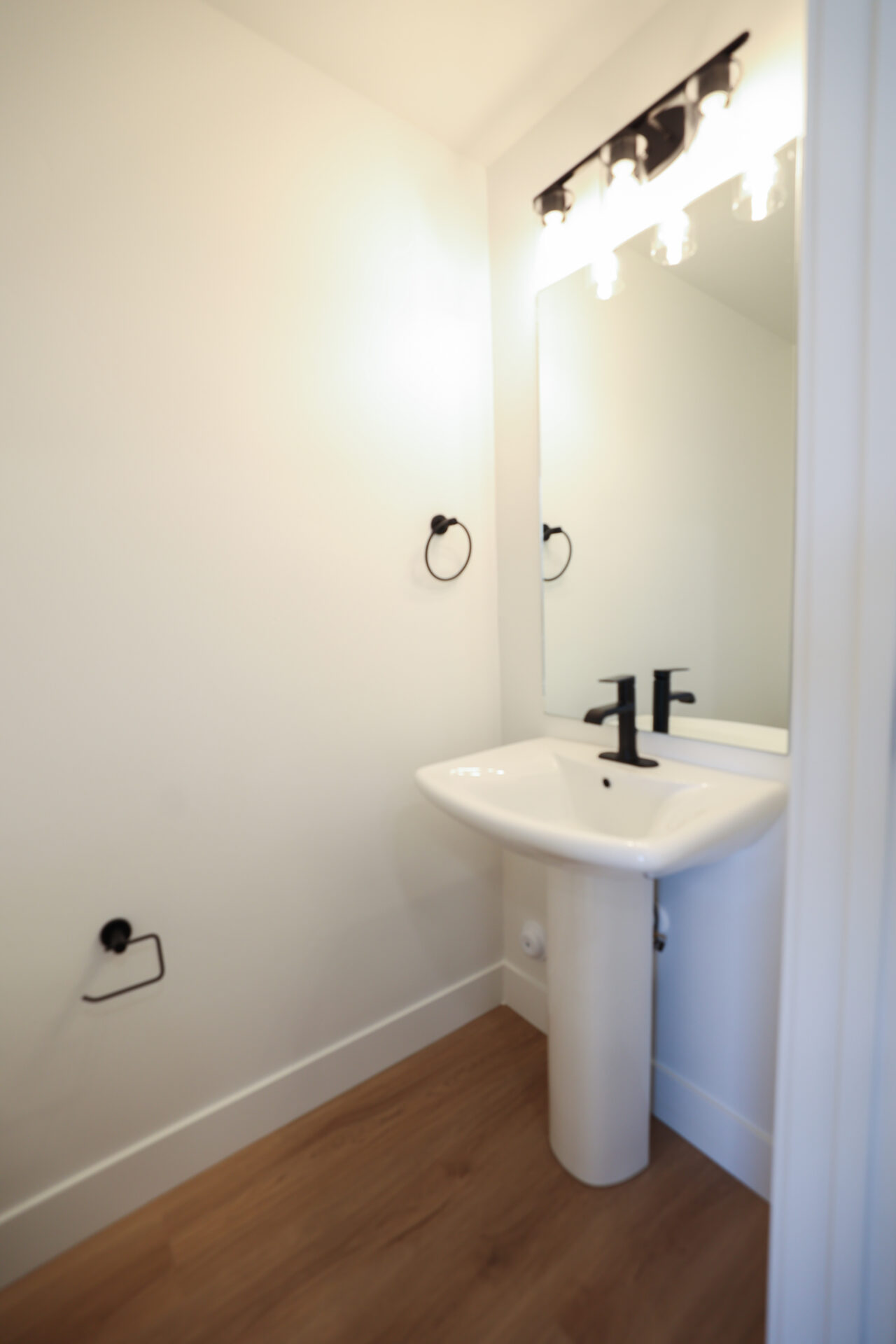 Pedestal sink with matte black faucet, framed mirror, and coordinating matte black towel ring