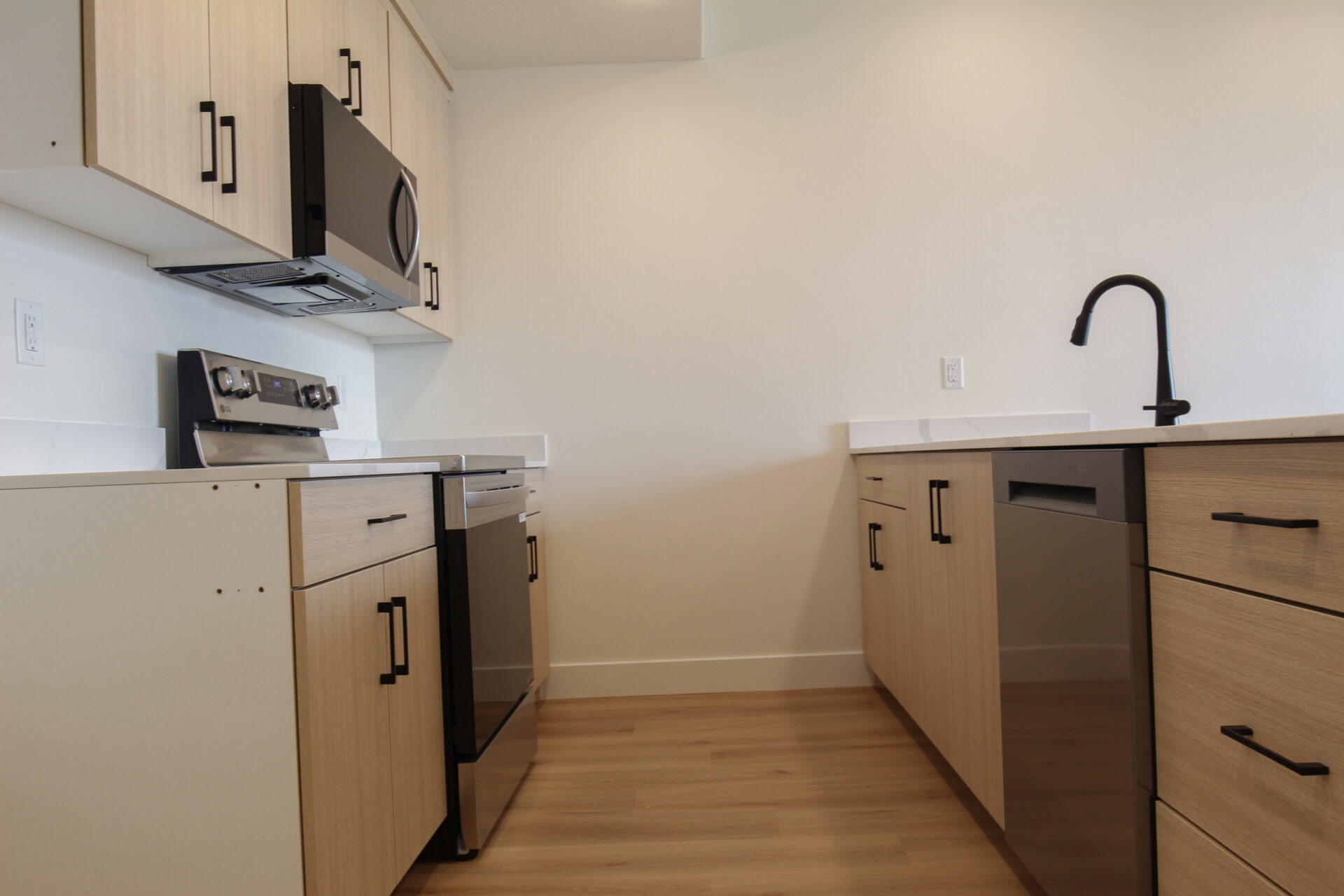 Kitchen featuring light wood-finish cabinetry, stainless steel appliances, a black gooseneck faucet, light countertops, and wood-finish flooring