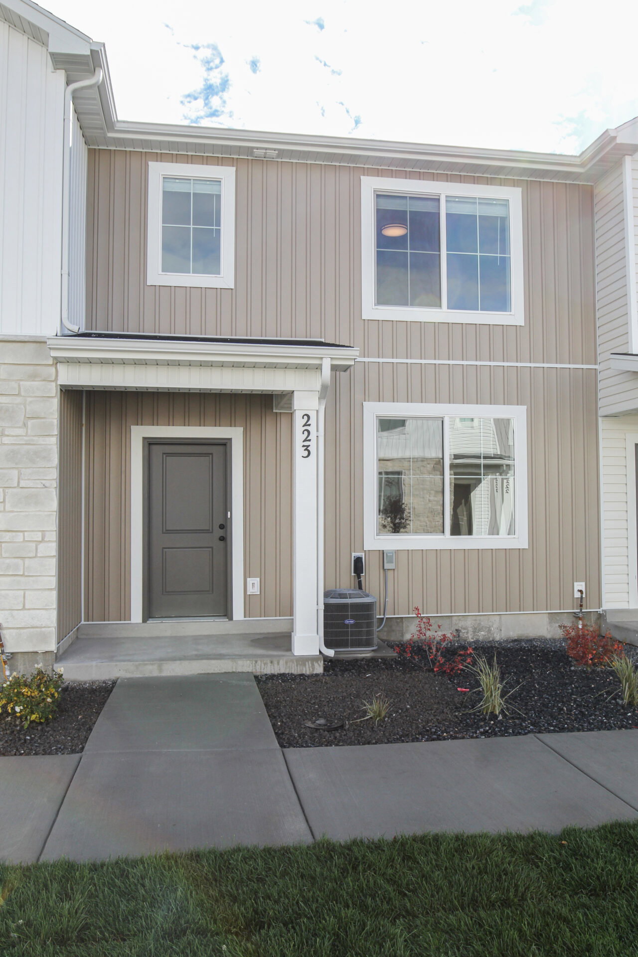 Contemporary townhouse exterior featuring a covered entry, vertical siding, stone veneer accents, multiple windows, and a paved walkway