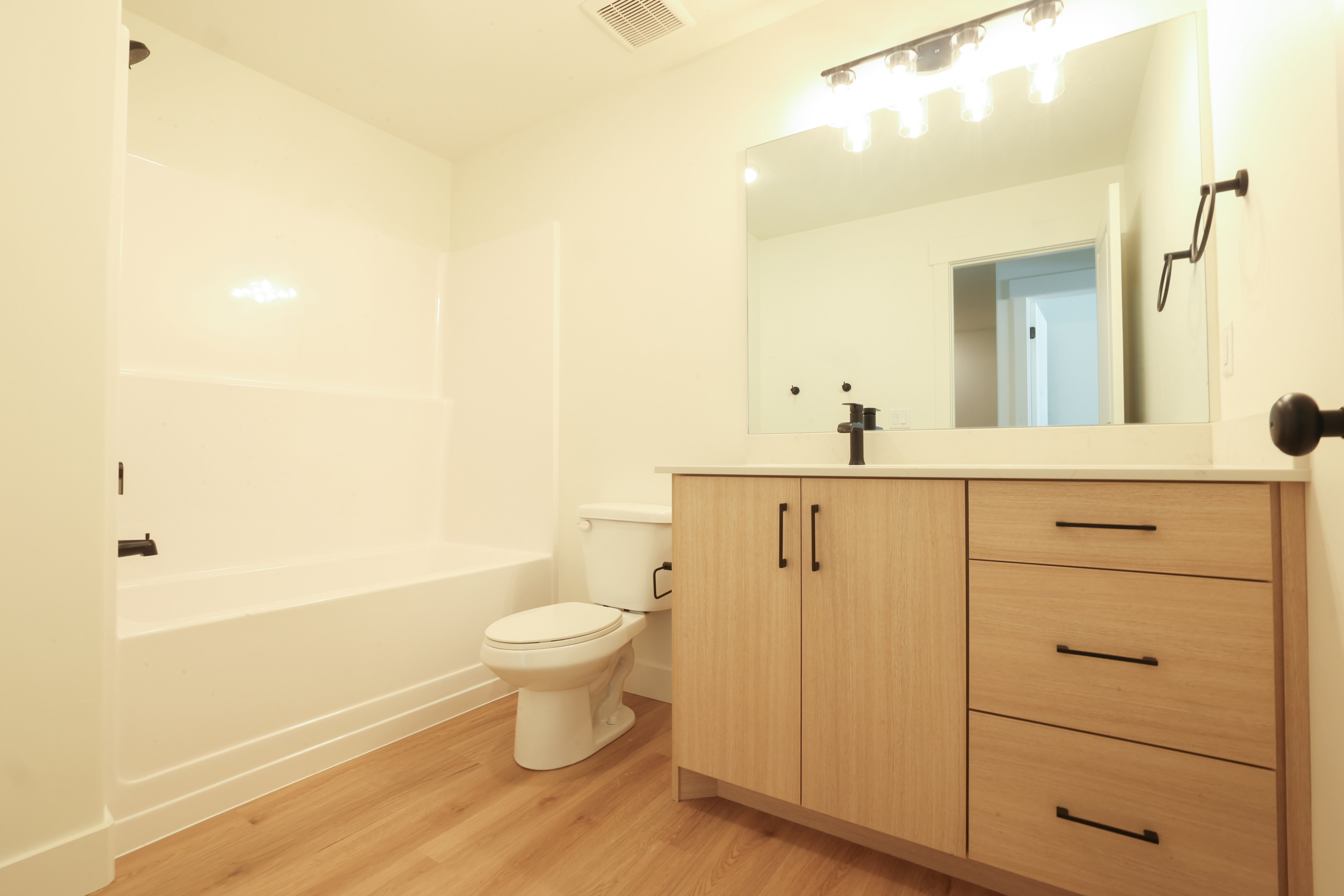 Bathroom featuring a light wood-finish vanity with a white countertop, matte black fixtures, and a large mirror with track lighting