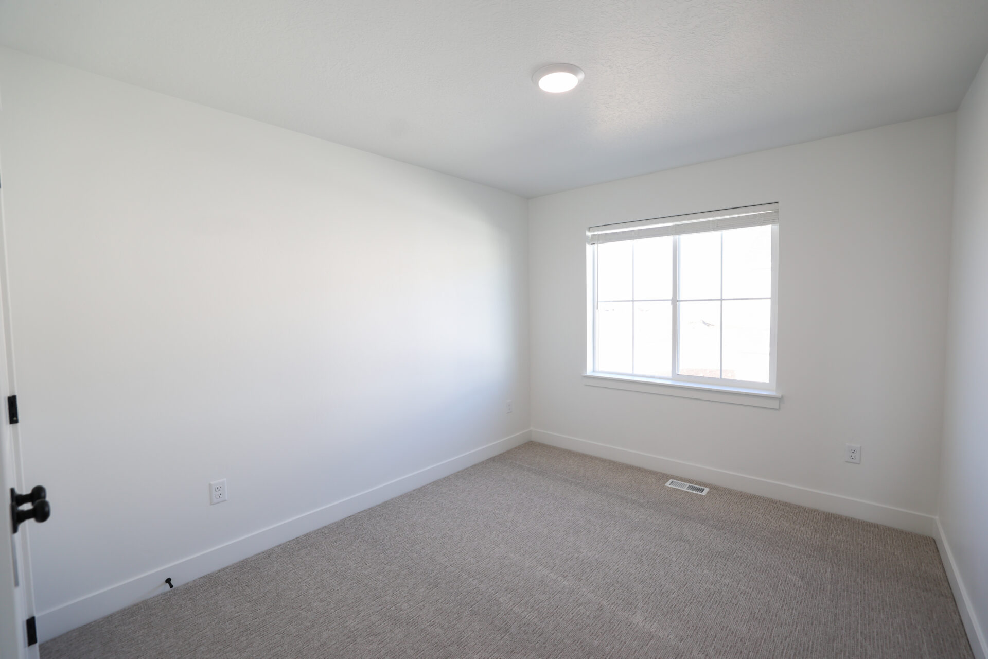 Neutral toned bedroom featuring light grey carpeting, white walls, and a recessed ceiling light