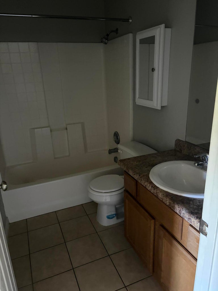 Bathroom featuring a white tub with shower surround, a white toilet, and tile flooring