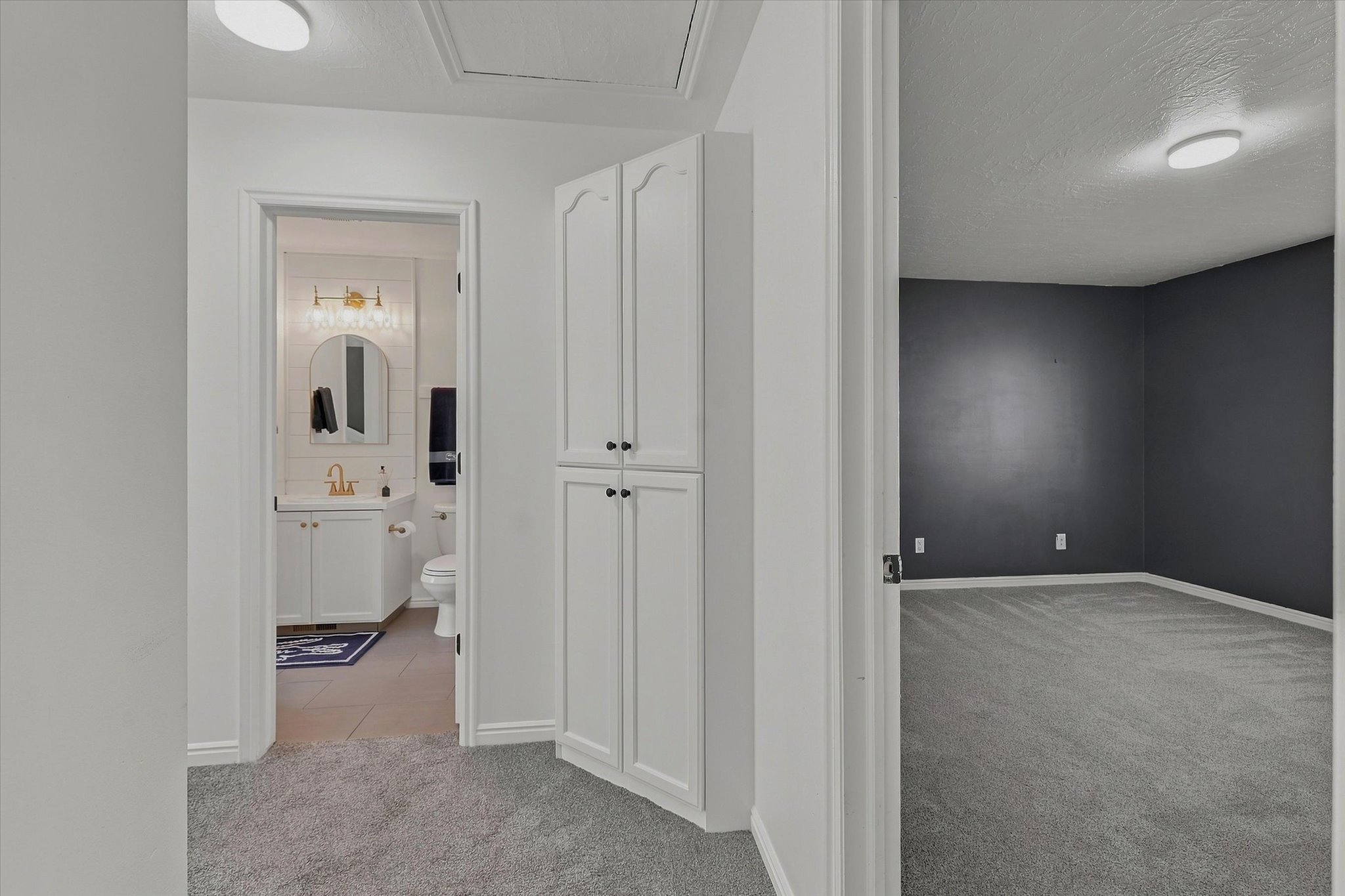 White built-in cabinetry provides storage in this hallway featuring grey carpet flooring
