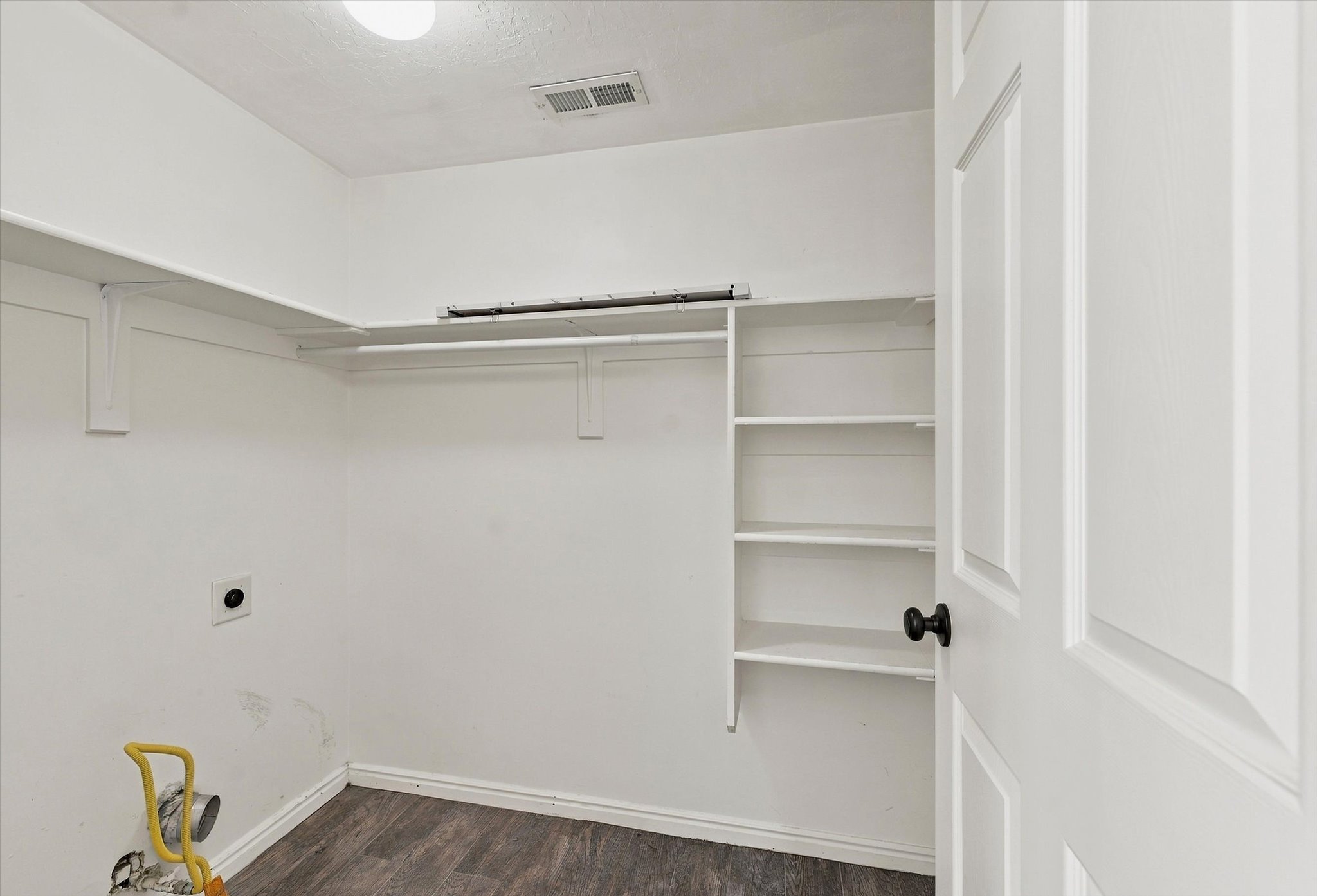 Laundry area featuring white walls, wood-finish flooring, a white paneled door with a matte black knob, and built-in shelving and hanging rods