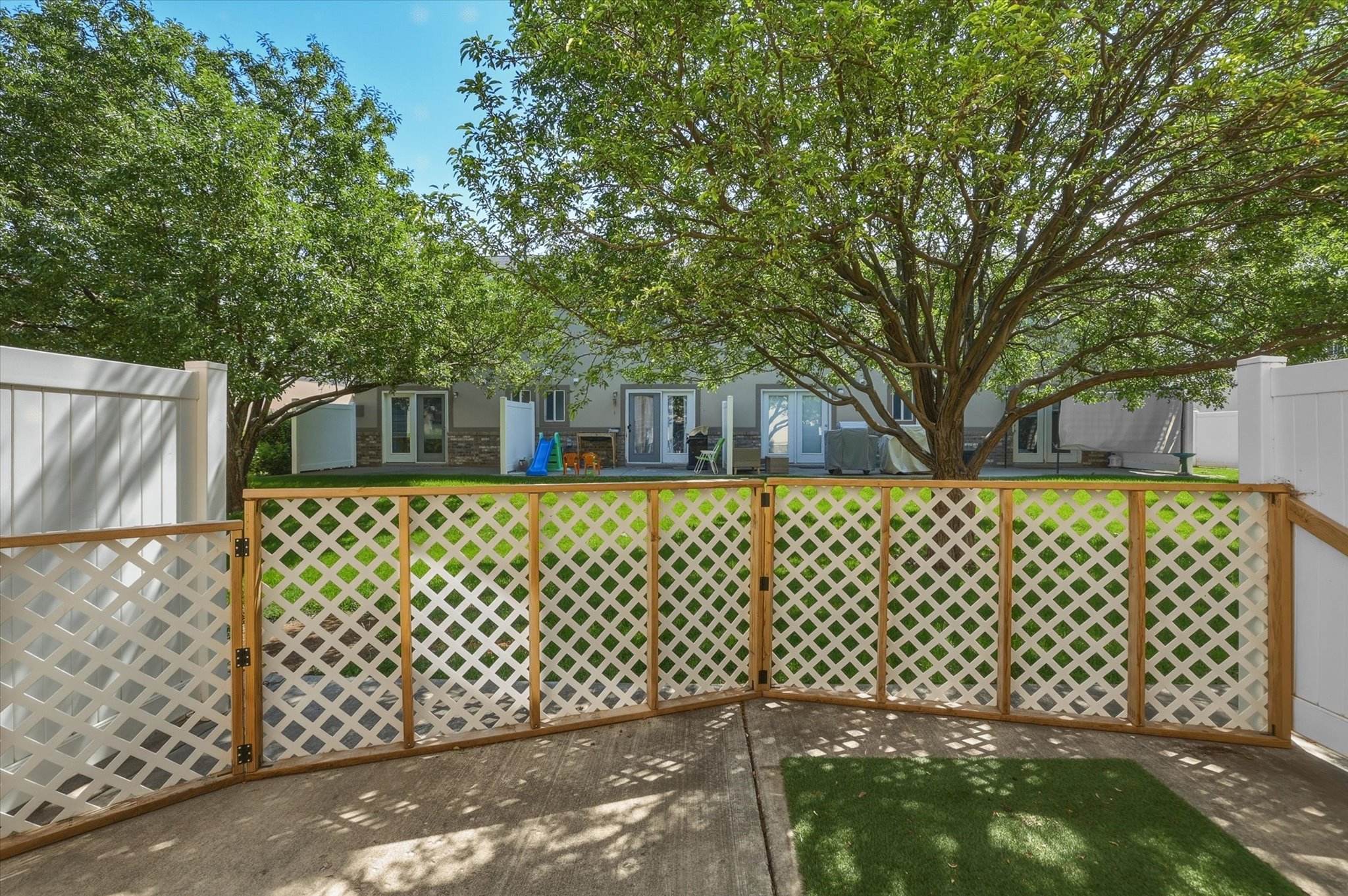 Patio area featuring concrete flooring, a lattice-style fence with a gate, and a section of artificial turf