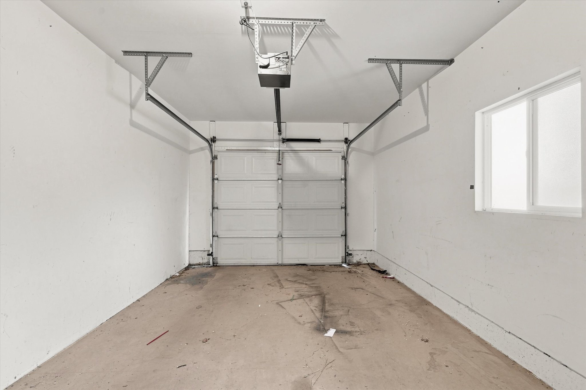Single-car garage featuring a roll-up door, automatic opener, concrete flooring, and a window for natural light
