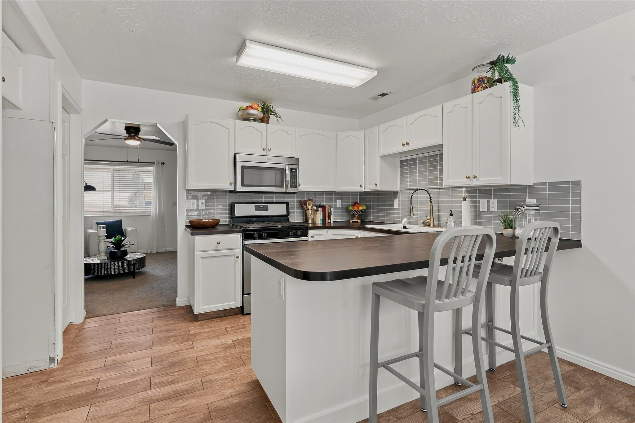 Kitchen featuring white cabinetry, grey subway tile backsplash, stainless steel appliances, a breakfast bar, and wood-finish flooring