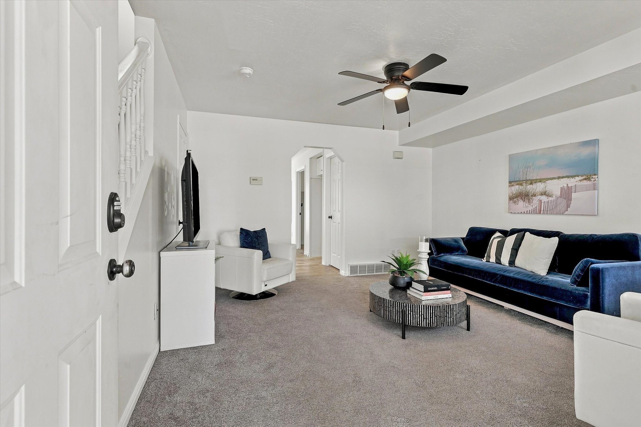 Carpeted living area featuring a ceiling fan with integrated lighting, white painted walls, white trim, and an archway leading to another room