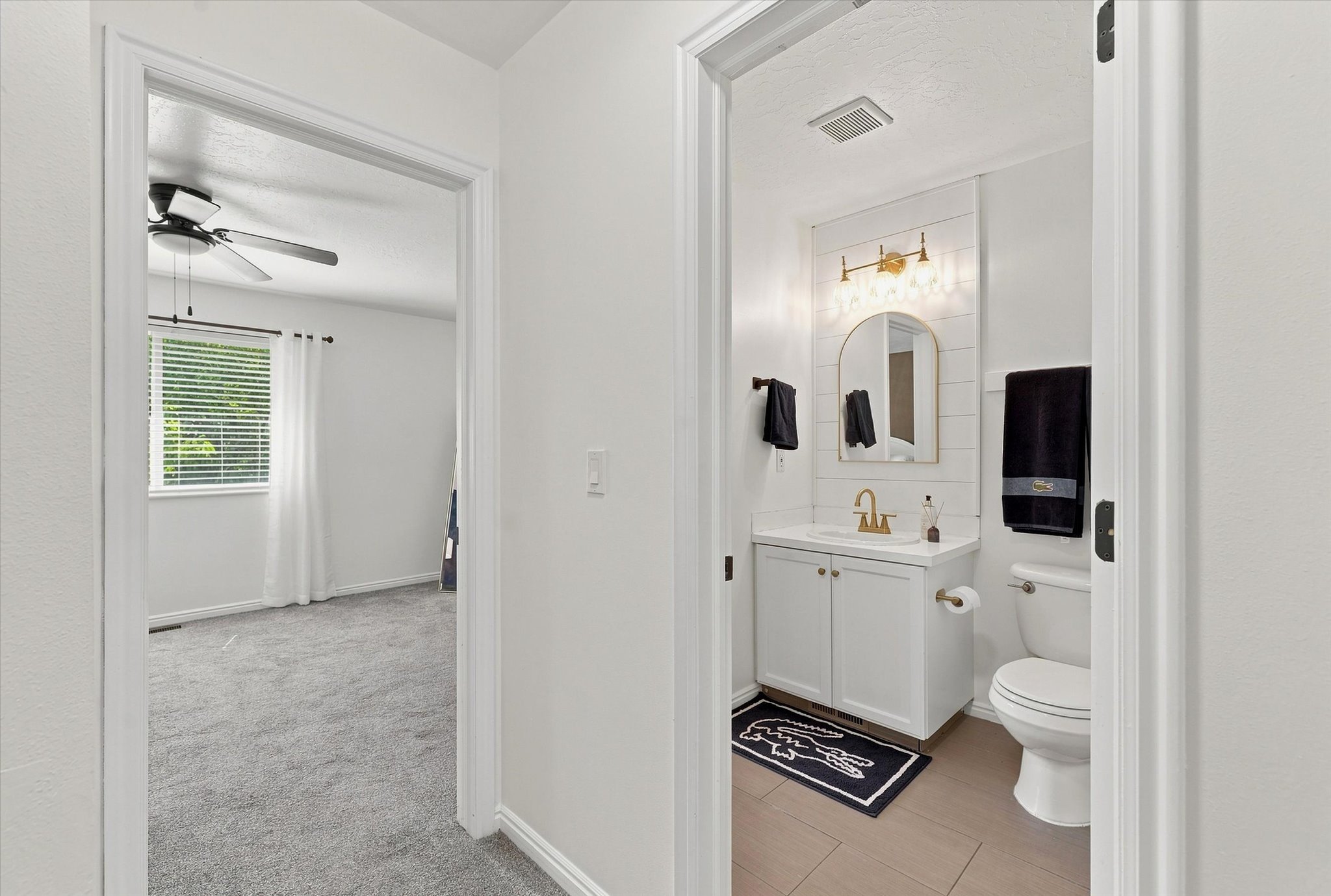 Bathroom featuring a white vanity with a gold-toned faucet, an arched mirror, and a tiled accent wall