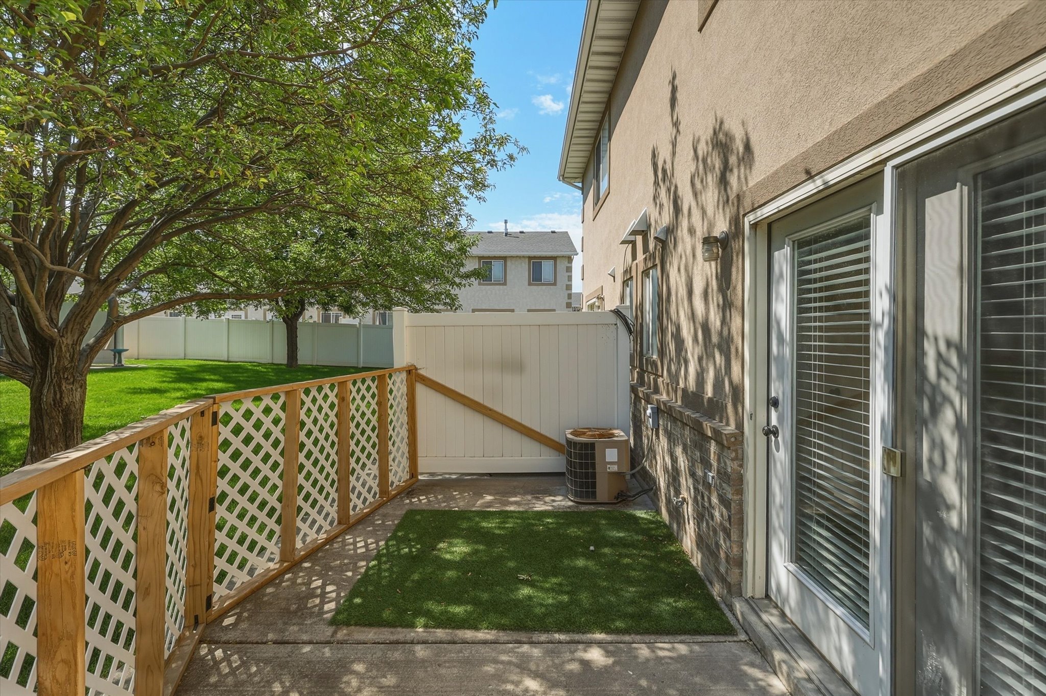 Private concrete patio featuring a faux turf accent, lattice fencing, and direct access to the interior