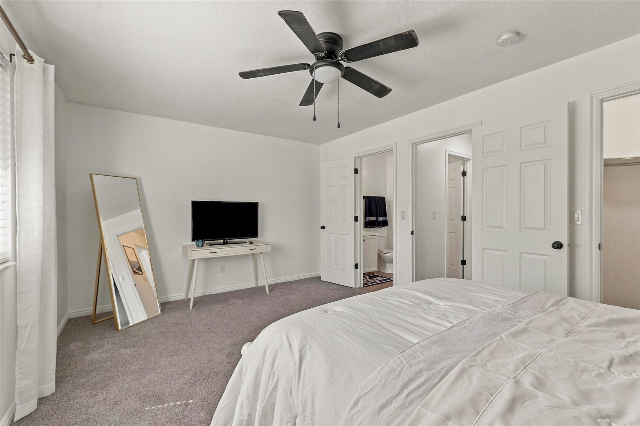 Spacious bedroom featuring neutral carpeting, a ceiling fan, and white walls
