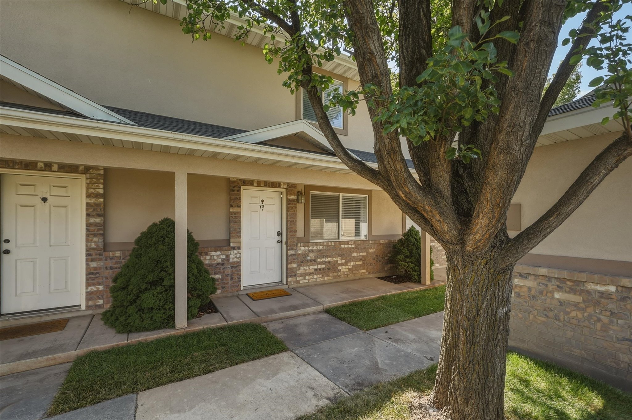 Exterior entry featuring two white panel doors, beige stucco siding, and a brick veneer foundation