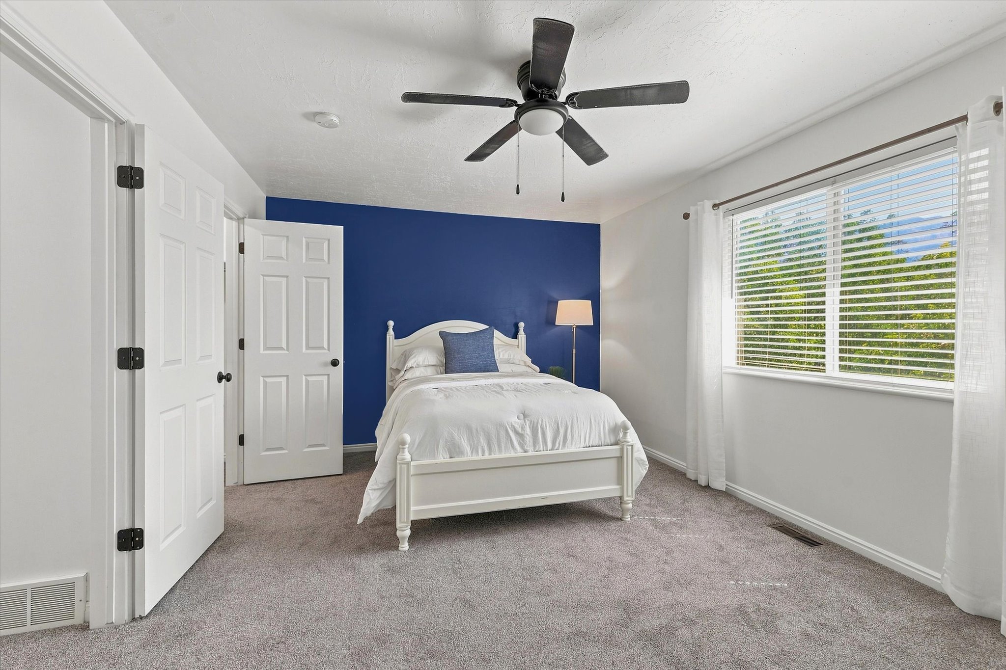 Interior room featuring a large window with white blinds, a ceiling fan with light fixture, and two white paneled doors