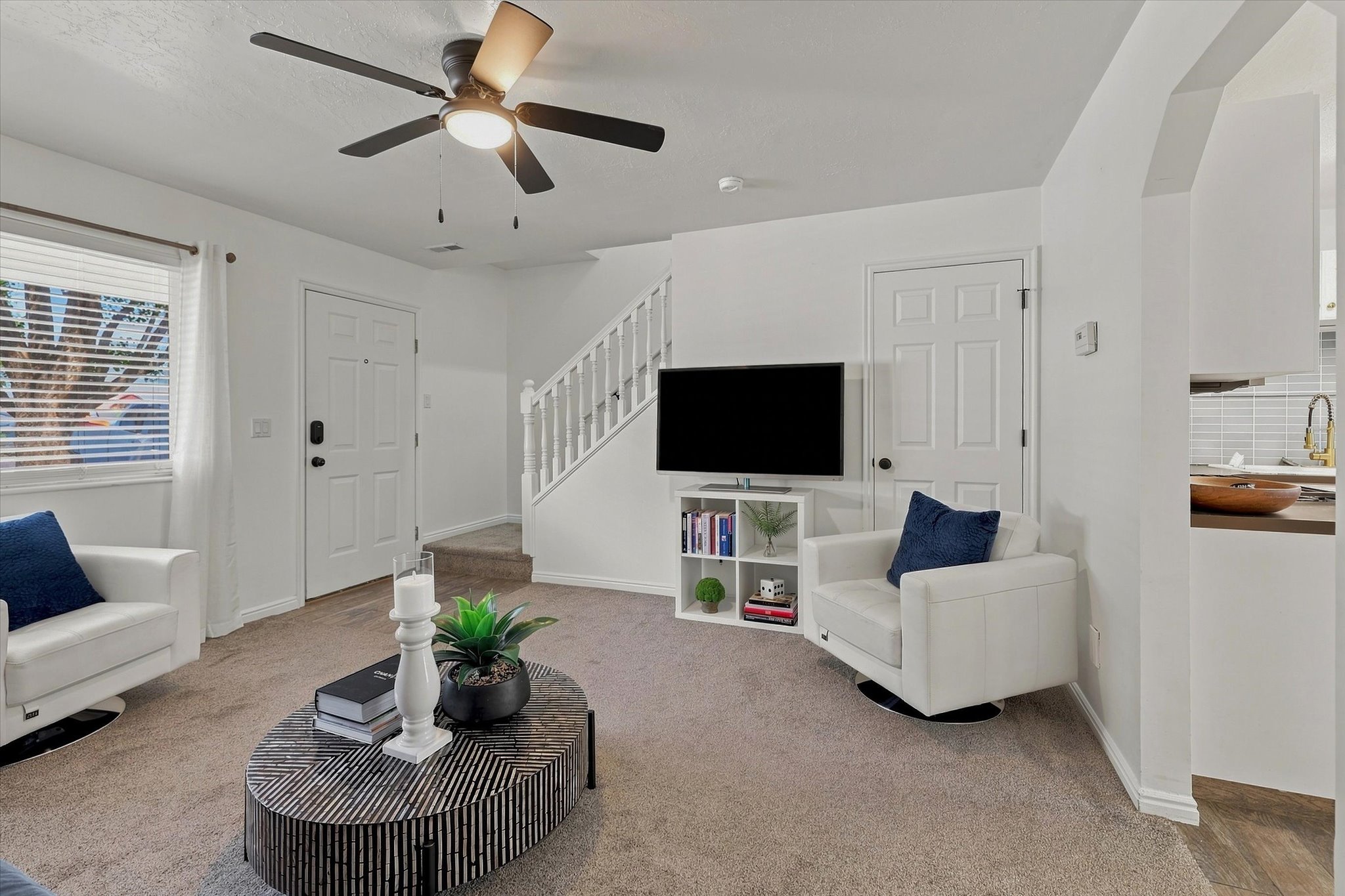 Carpeted living area featuring a ceiling fan with light, white trim, and a window with blinds