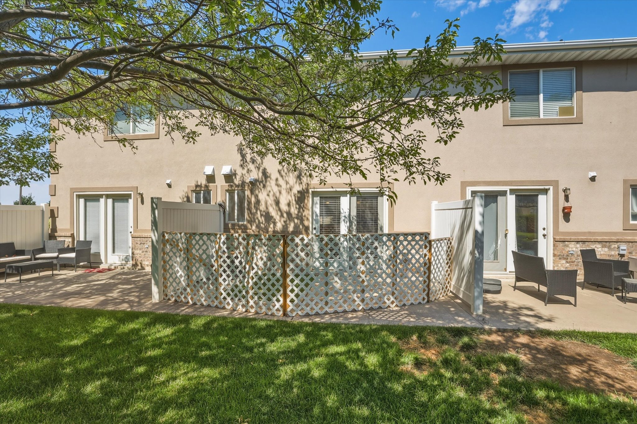Rear exterior featuring two private patio areas, stucco facade, stone accents, multiple sliding glass doors, and upper-level windows