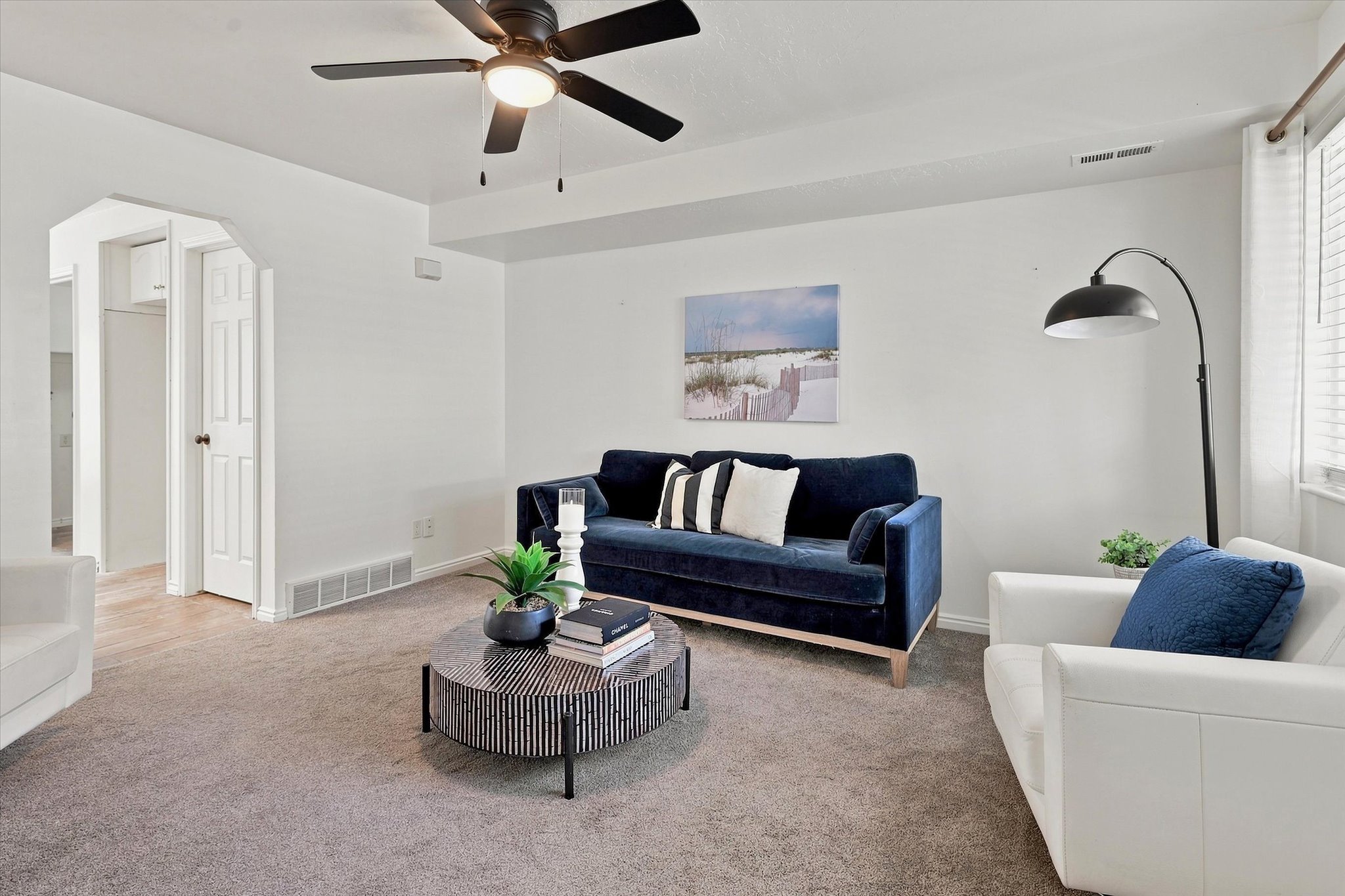 Carpeted living area featuring a ceiling fan with integrated lighting, white walls, and an arched doorway