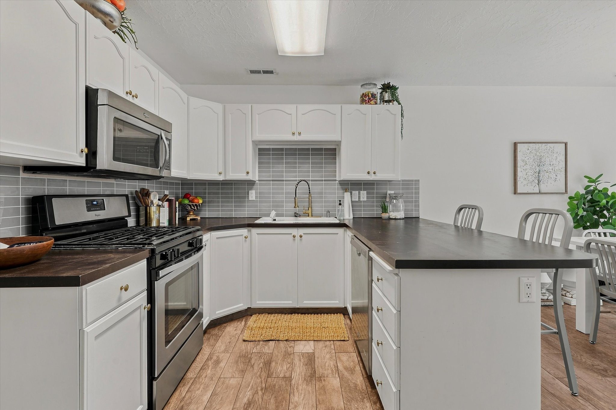 White cabinetry with gold-tone hardware, wood-finish flooring, stainless steel appliances, dark countertops, and a gray subway tile backsplash