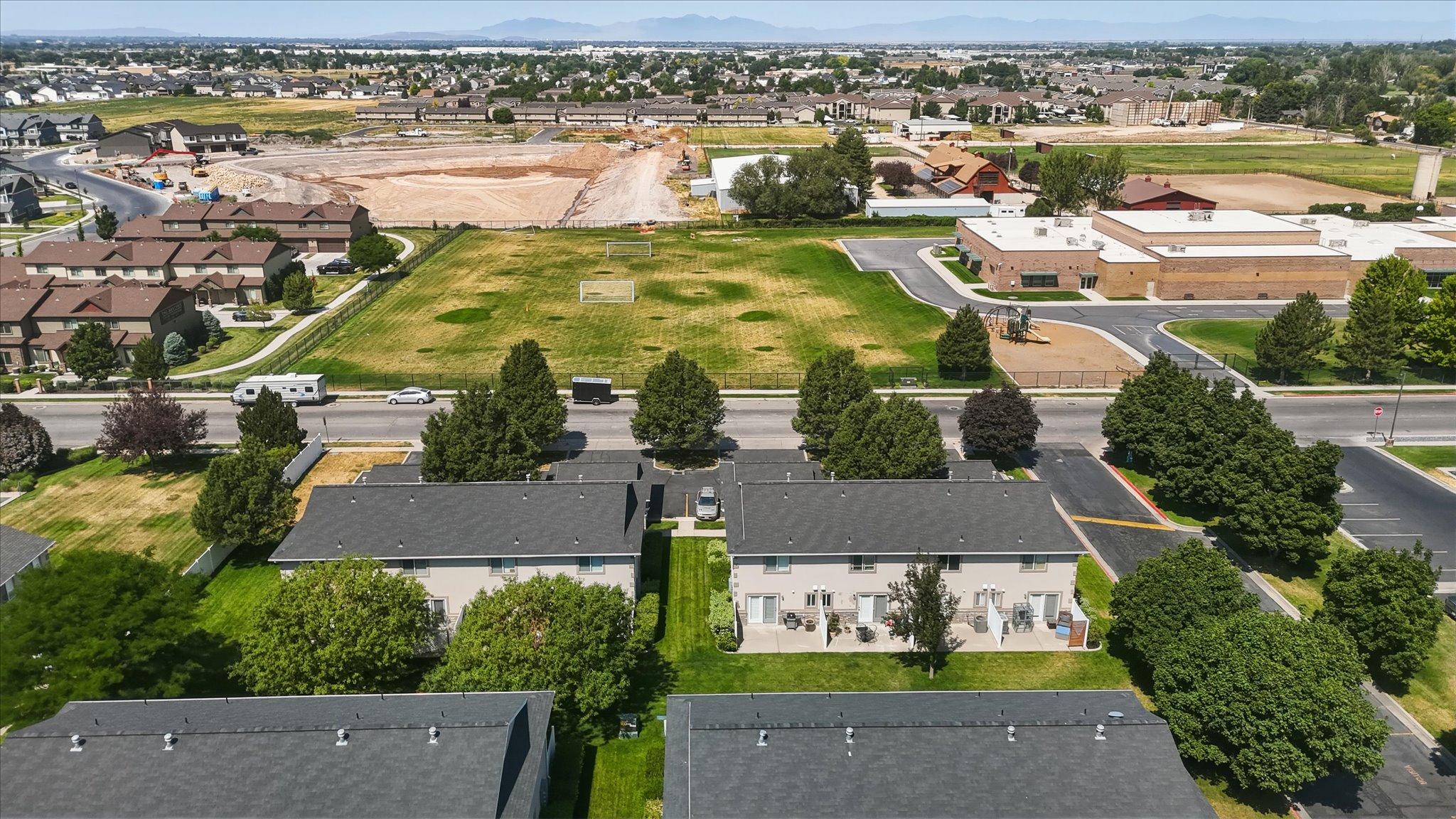 Aerial perspective showcasing multiple properties with dark shingle roofs, surrounded by green lawns and mature trees