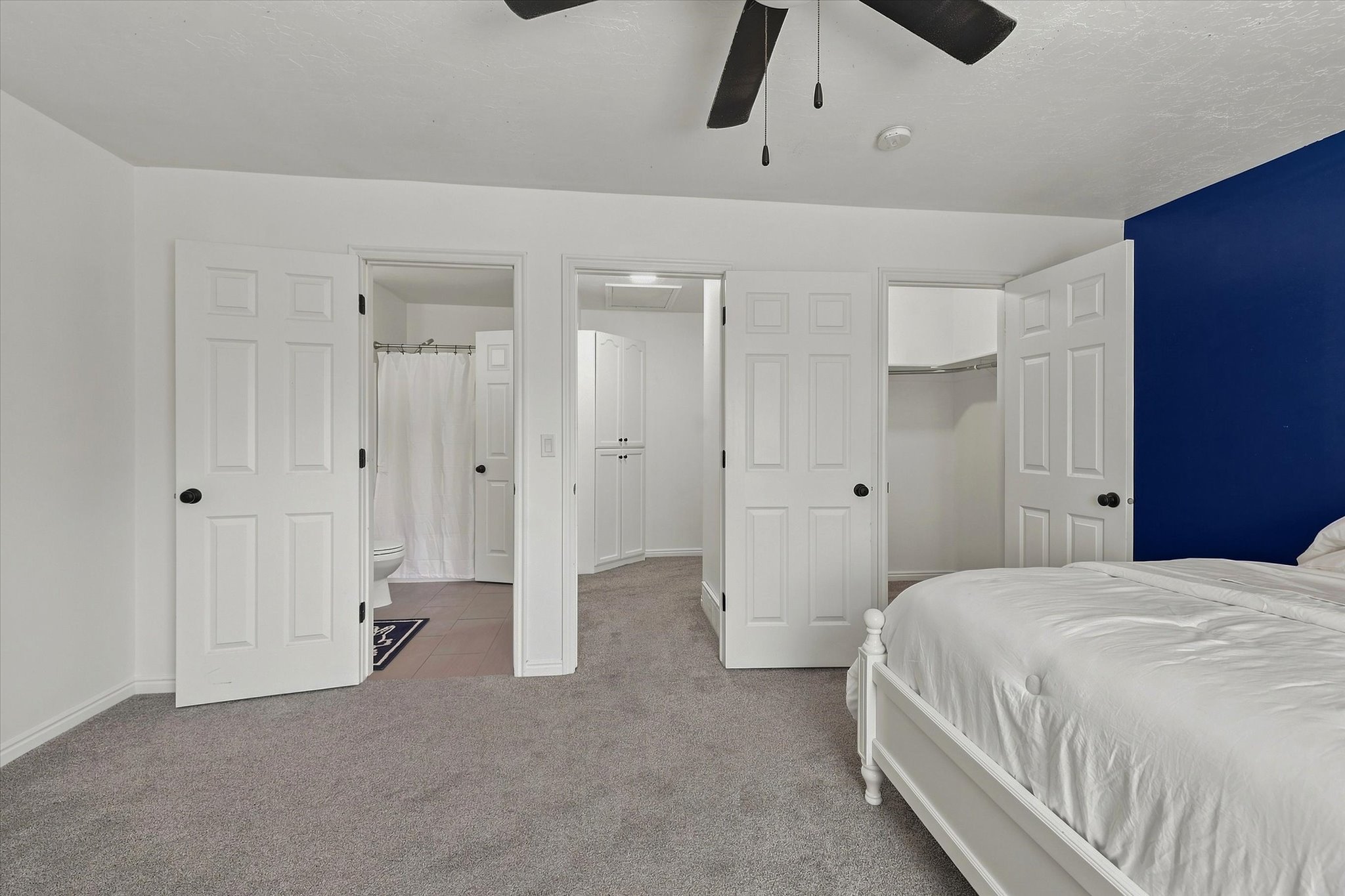 Spacious carpeted room featuring a ceiling fan, a distinct accent wall, and multiple white six-panel doors