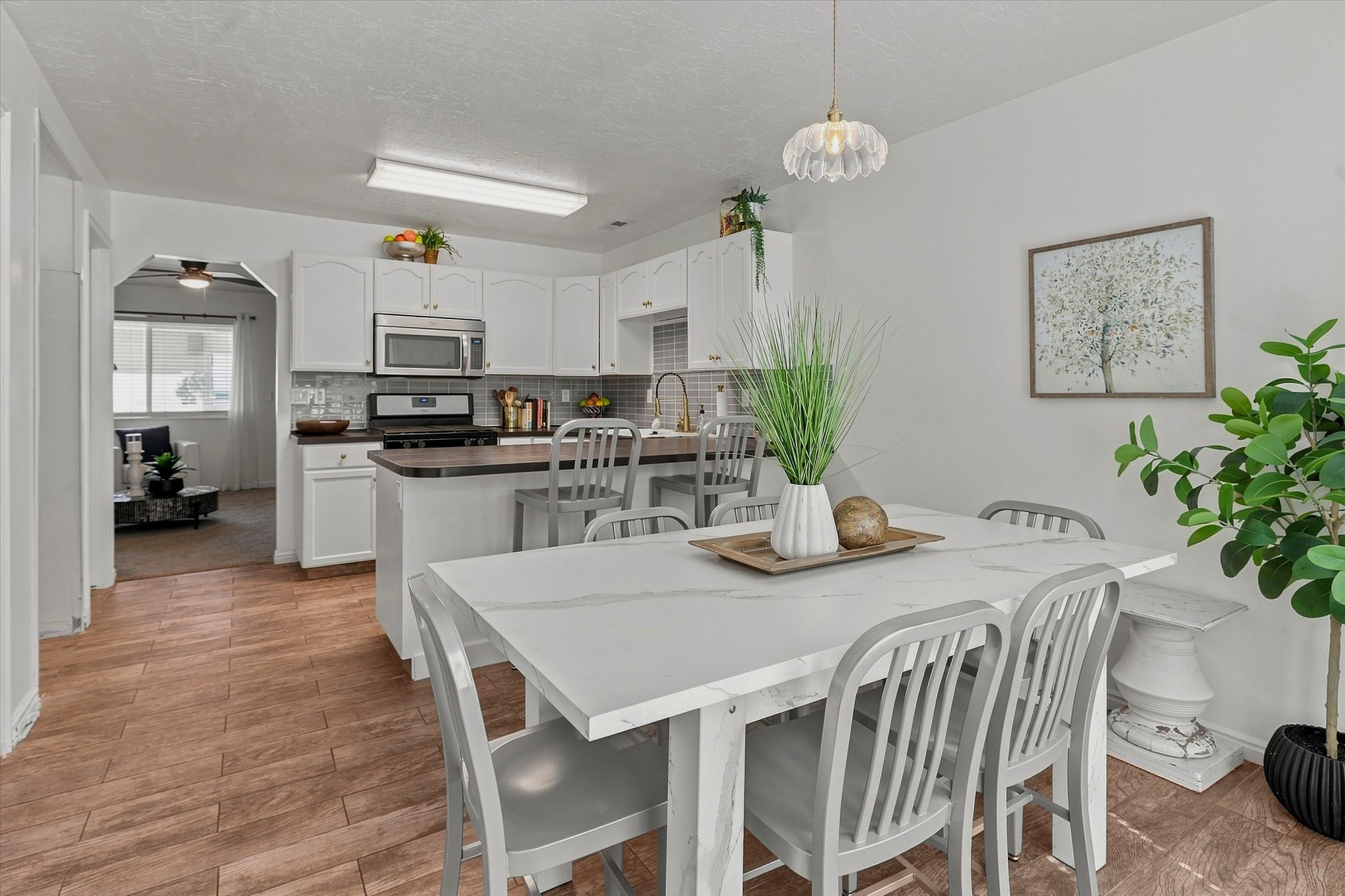 Open-concept dining area featuring wood-finish flooring, a white dining table, and a contemporary pendant light fixture