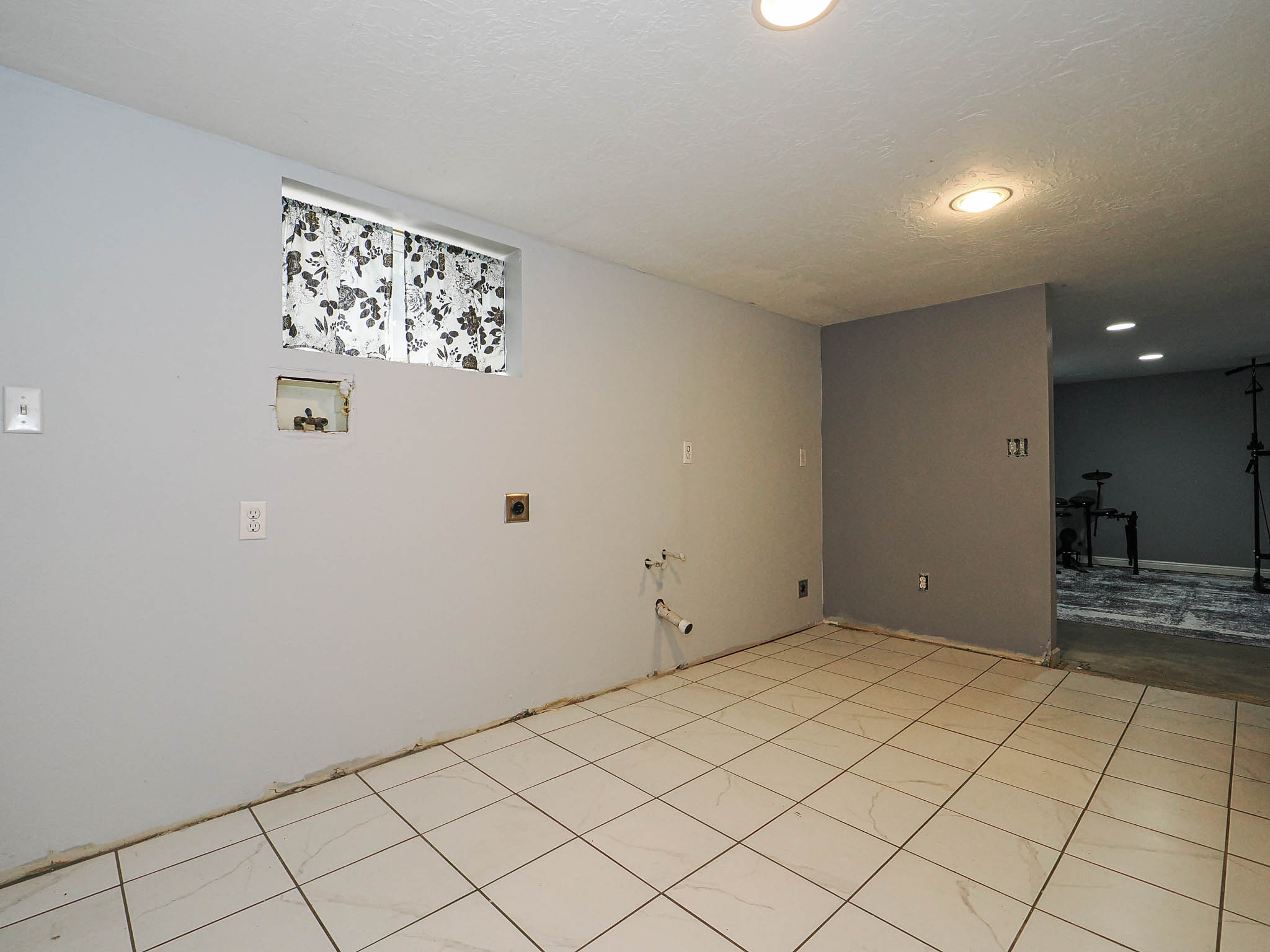 Room featuring light-toned square floor tiles, recessed ceiling lighting, and a window with a patterned curtain