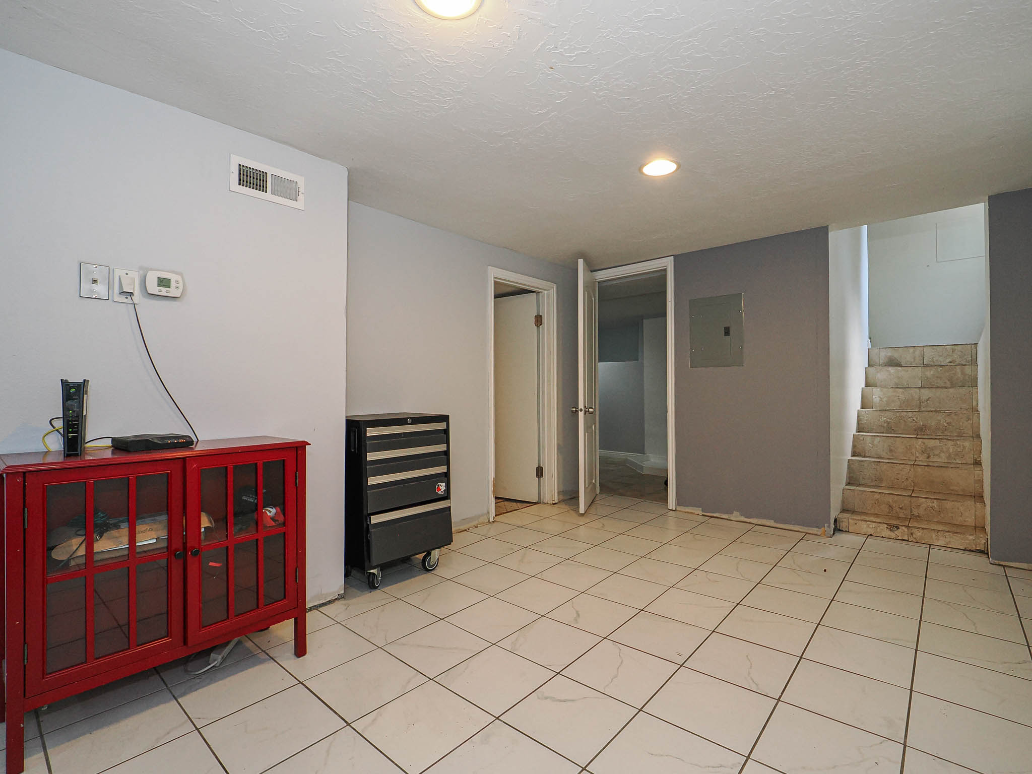 Spacious room featuring white tiled flooring, light gray and dark gray wall finishes, recessed lighting, and a visible air vent