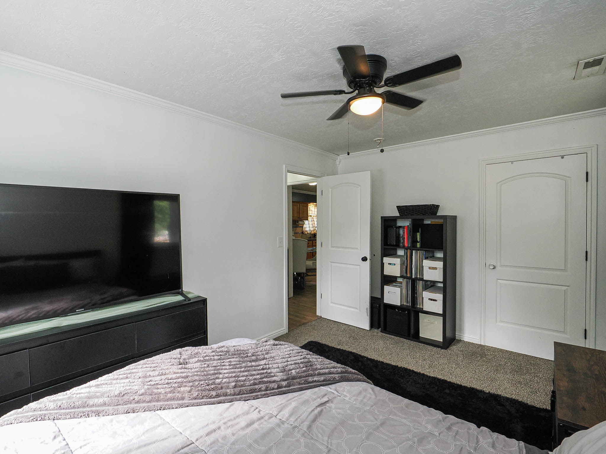 Bedroom featuring neutral wall paint, crown molding, a ceiling fan with light fixture, two panel-style doors, and carpet flooring