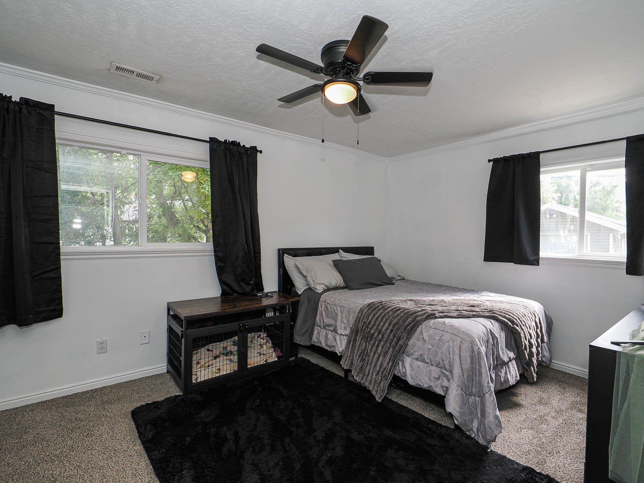 Bedroom featuring two windows with white trim, gray carpet, and a ceiling fan with integrated lighting