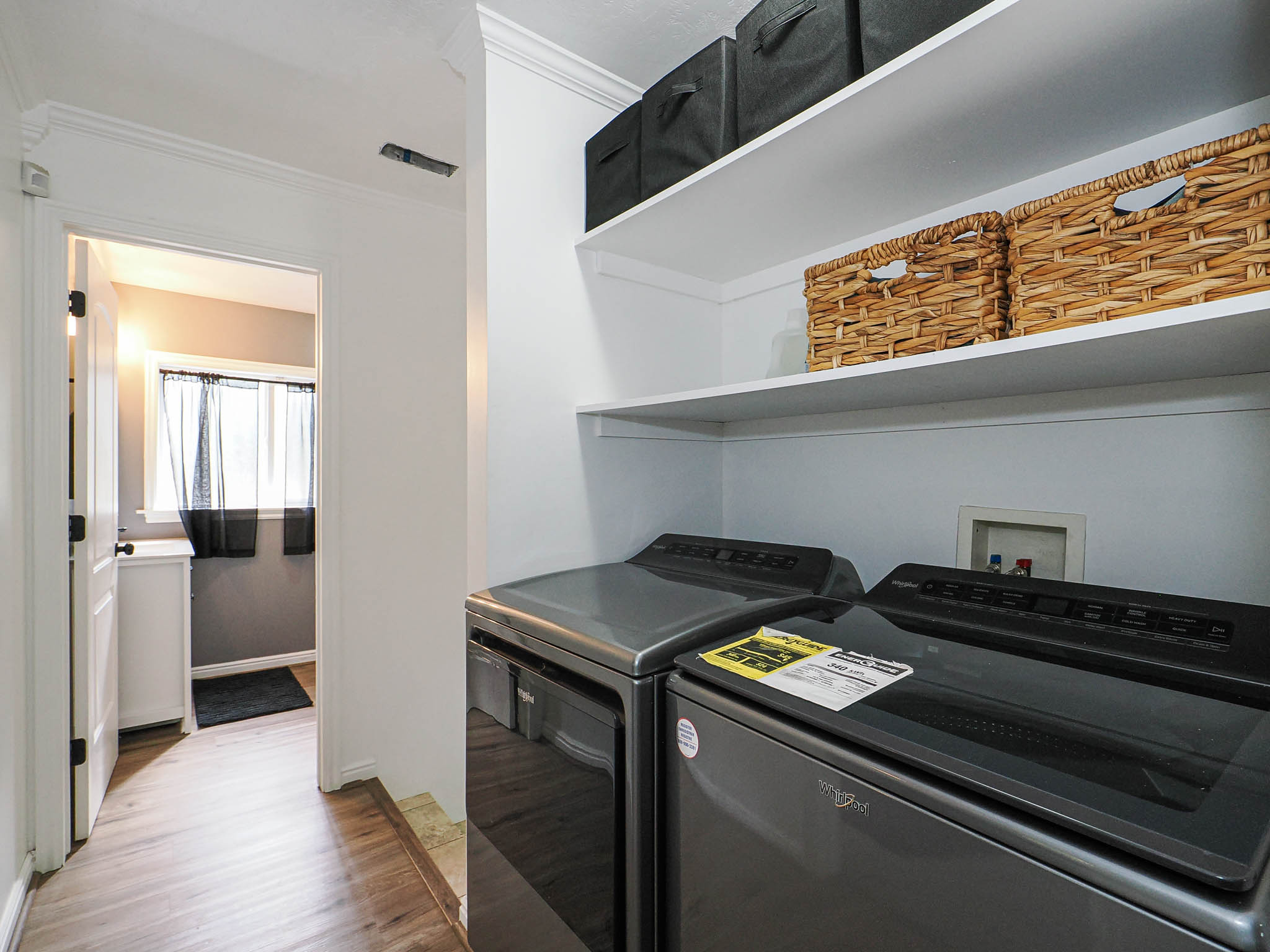 Dedicated laundry area featuring dual built-in shelving, white walls, and wood-finish flooring