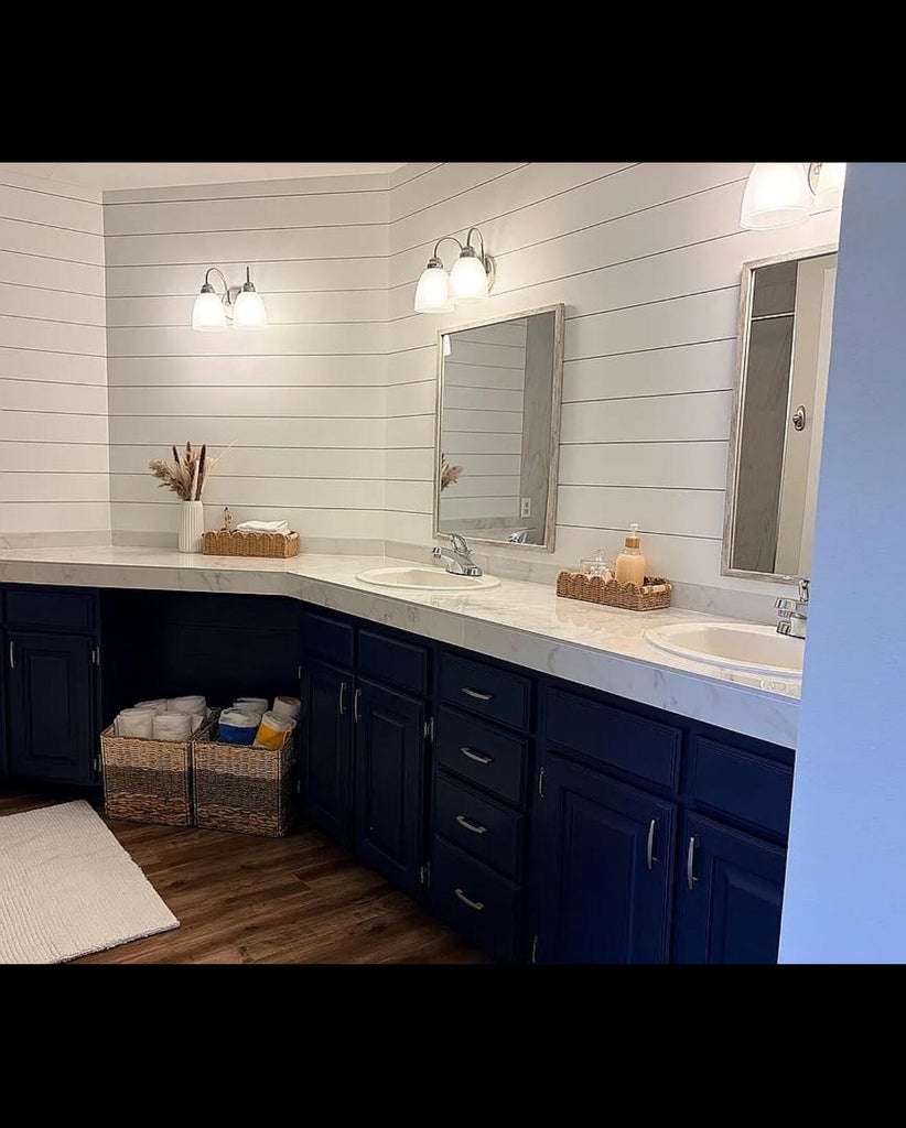 Double vanity with undermount sinks and chrome fixtures, contrasting navy cabinetry, white shiplap walls, and wood-finish flooring