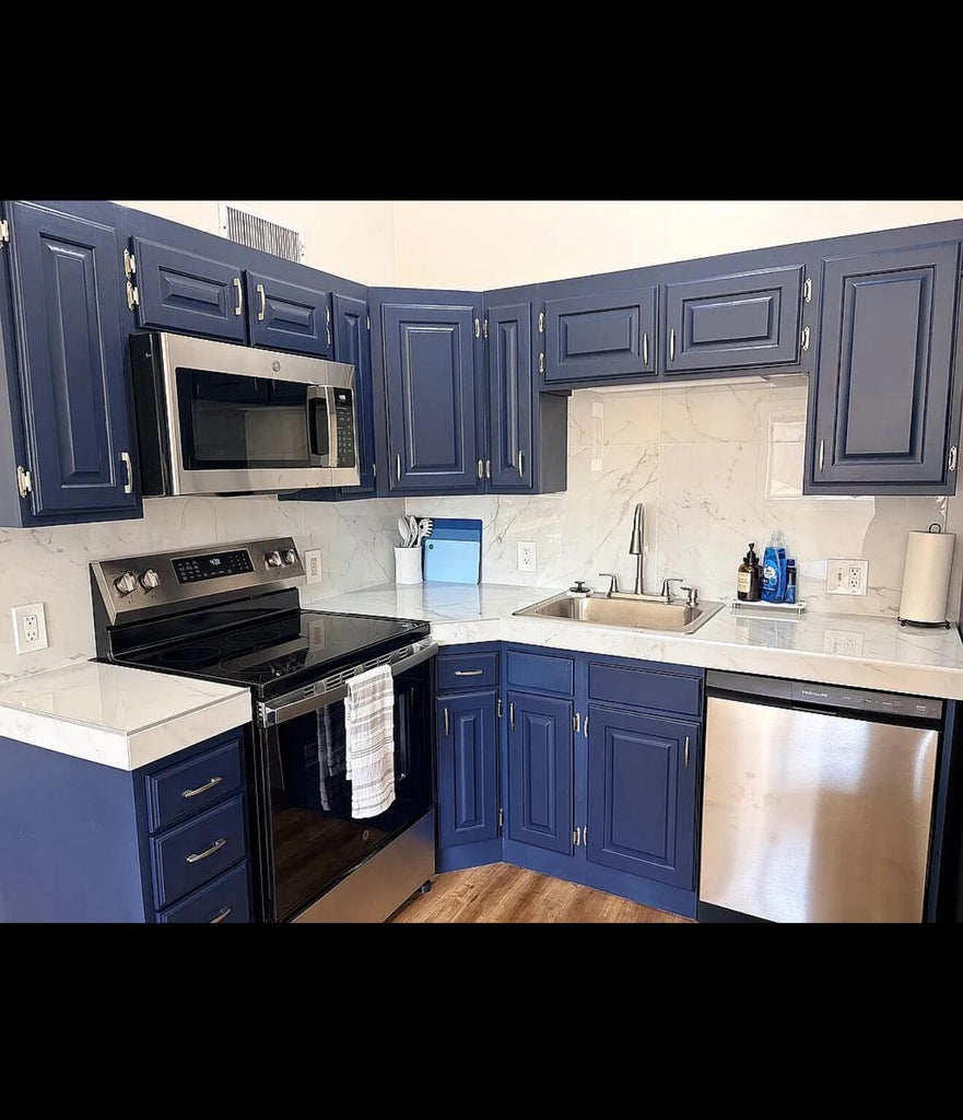 Kitchen featuring navy cabinetry with panel detailing, light-toned countertops, a stainless steel over-the-range microwave, a stainless steel electric range, and a stainless steel dishwasher