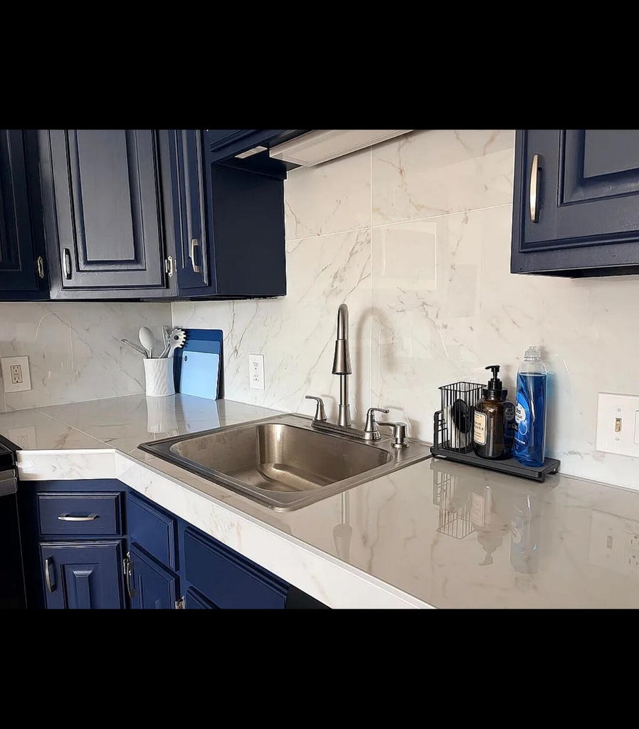 Kitchen featuring a stainless steel undermount sink, gooseneck faucet, light-toned countertops, and a white marble-patterned tile backsplash
