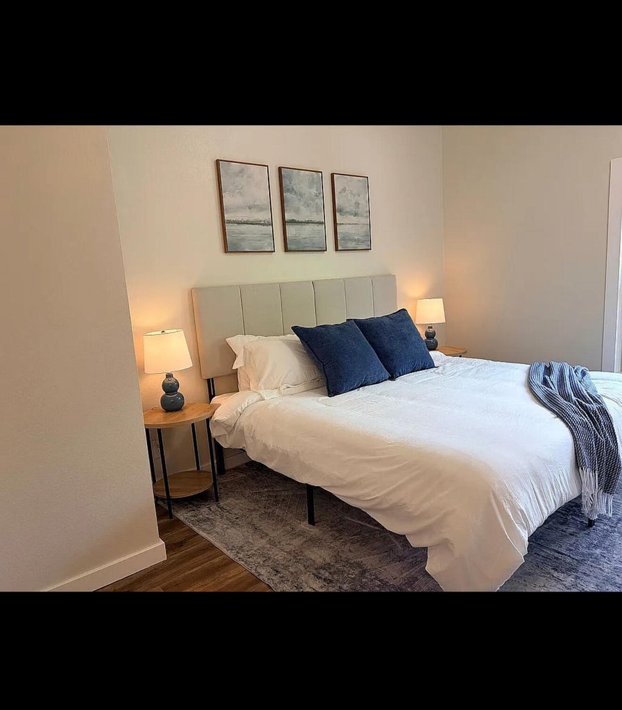 Bedroom featuring wood-finish flooring, light-toned wall paint, and a built-in upholstered headboard