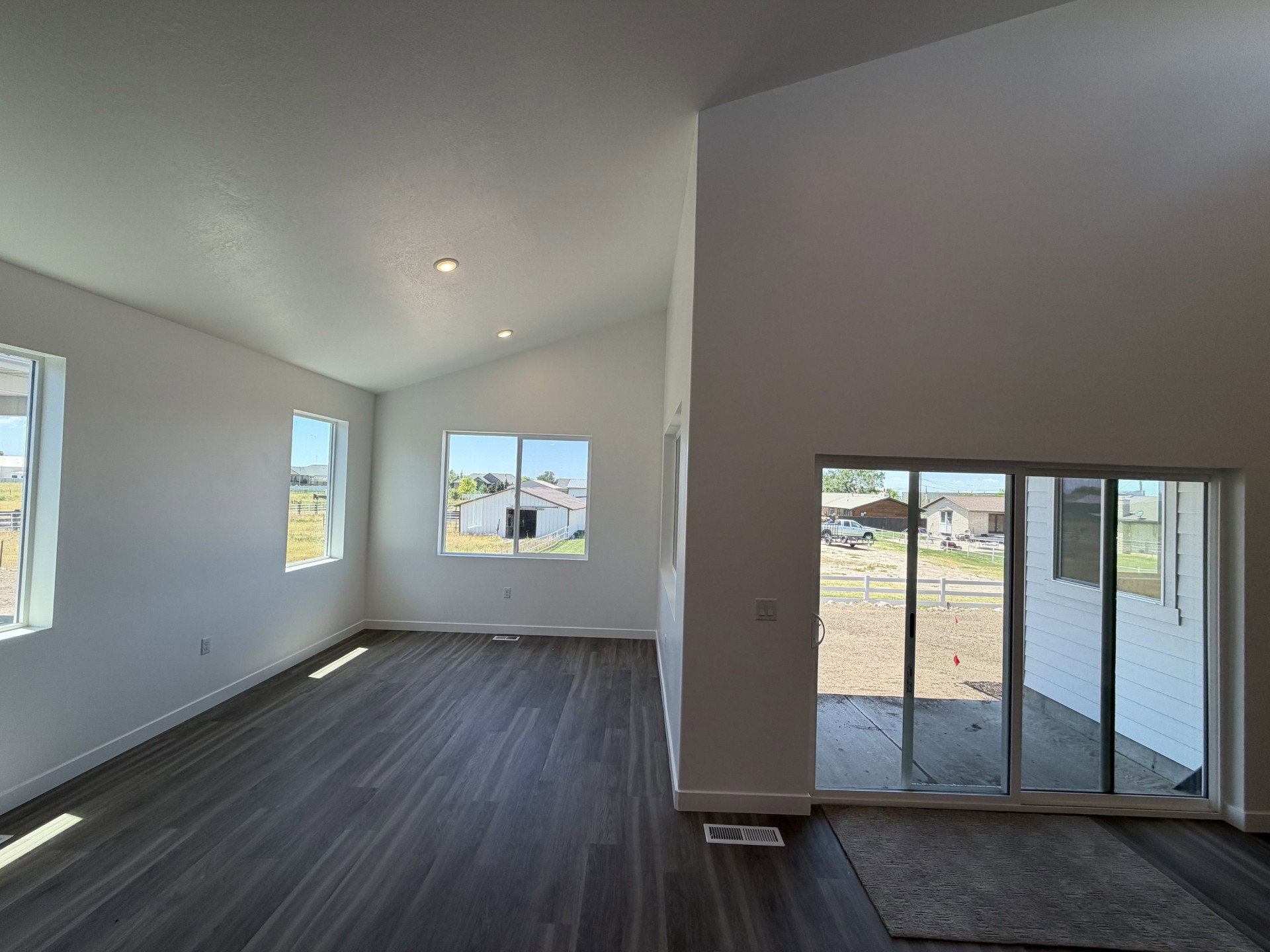 Spacious room featuring vaulted ceilings, recessed lighting, wood-finish flooring, multiple windows, and a sliding glass door