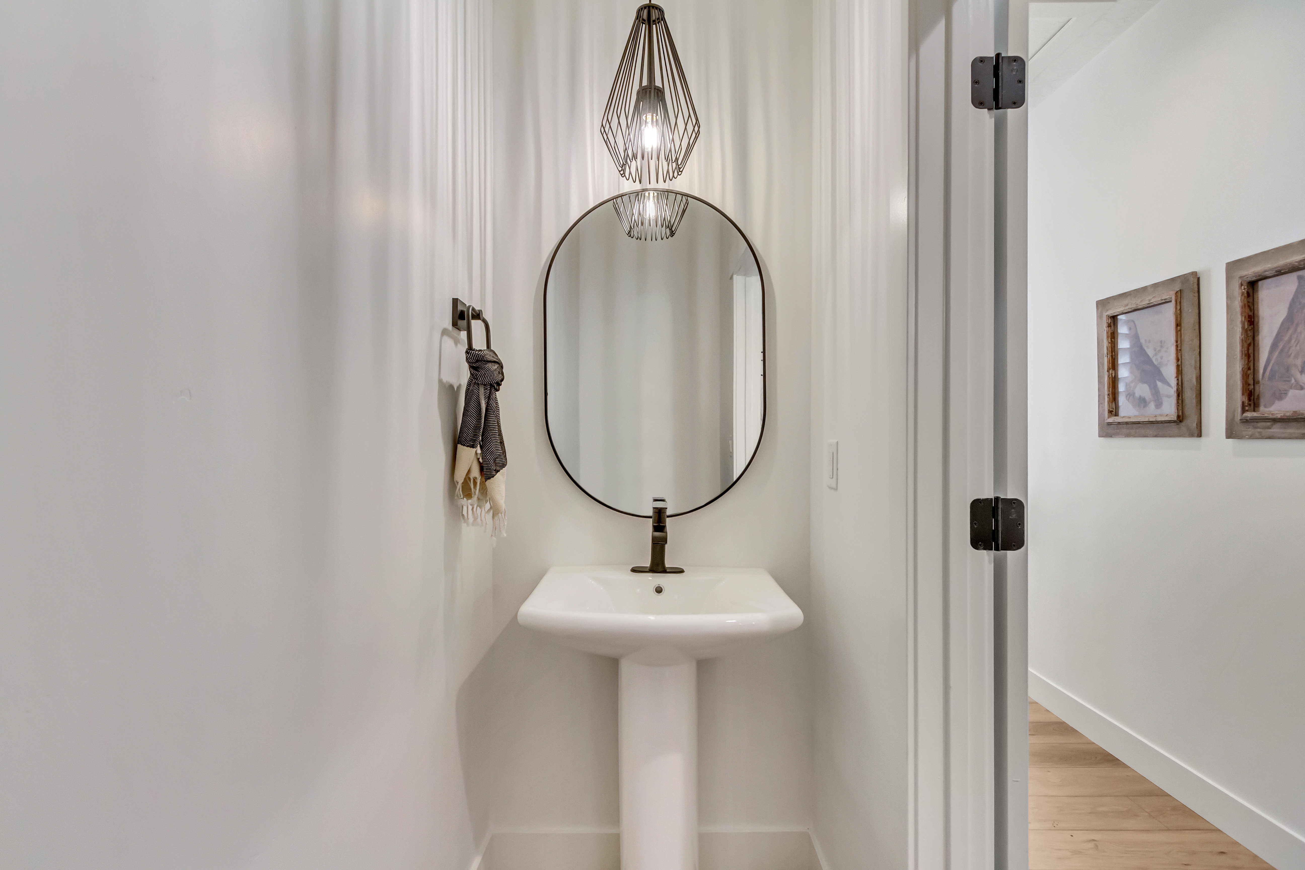 Pedestal sink with bronze-finish faucet, framed by an oval mirror