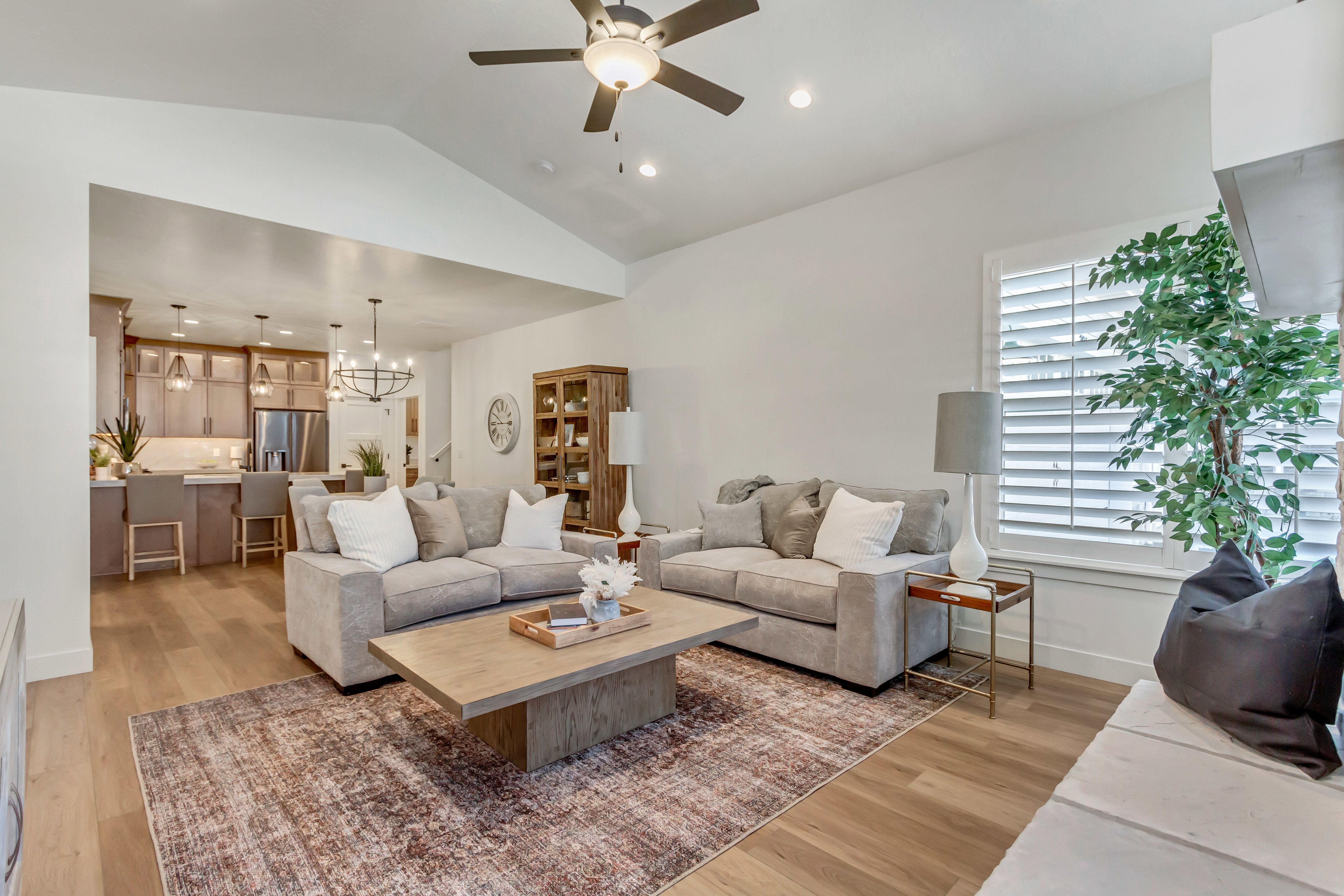 Spacious living area featuring vaulted ceilings with a ceiling fan, light wood-finish flooring, and white plantation shutters